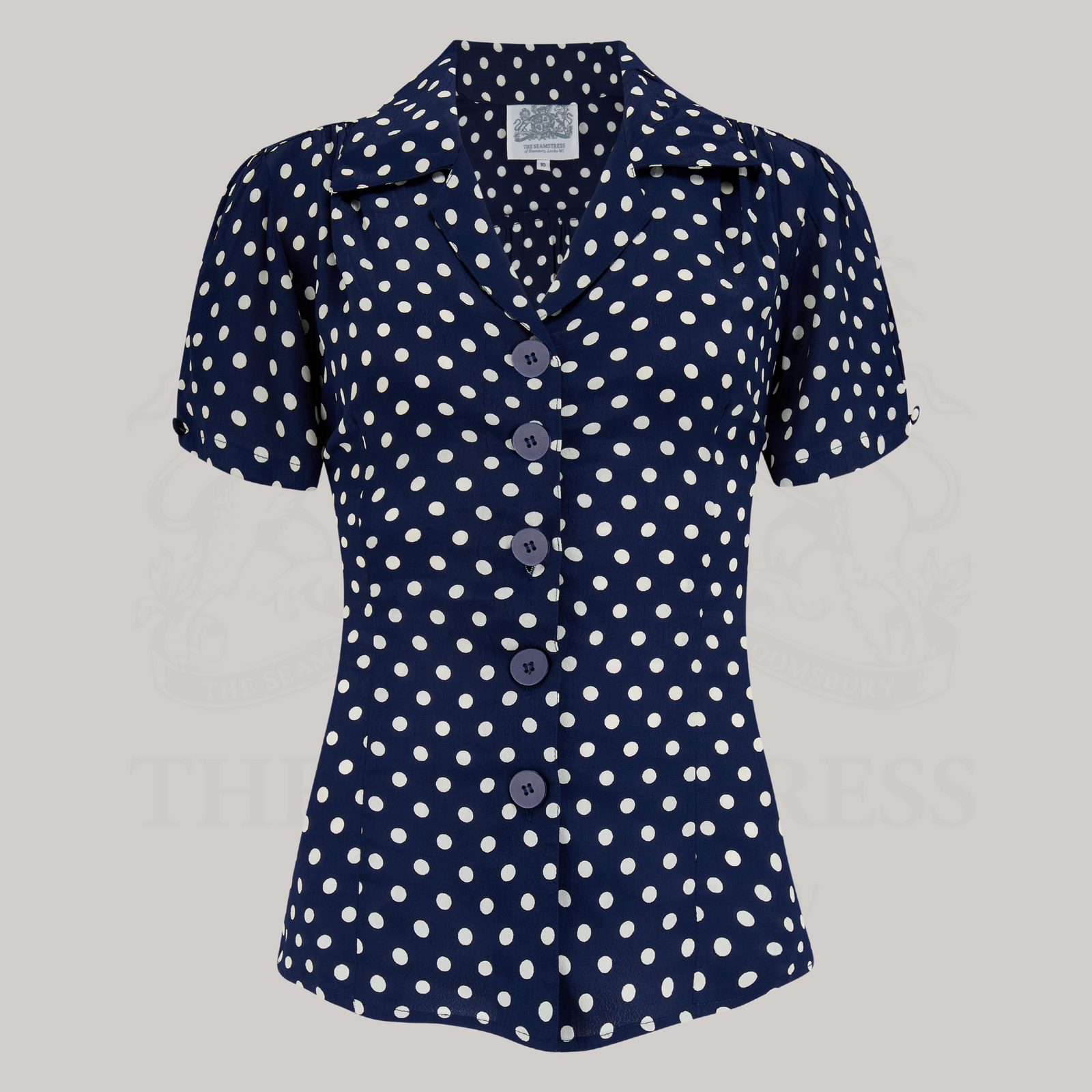 A navy crepe de chine blouse with white polka dots, featuring a classic revere collar, large bakelite buttons, and short sleeves.
