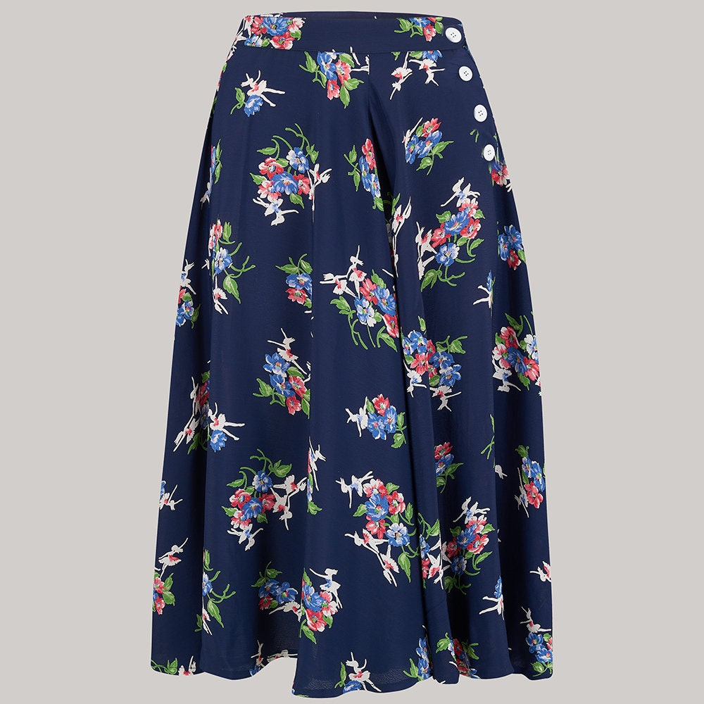 A navy blue midi skirt with a colourful floral and white dancer print, featuring a buttoned waistband, shown against a solid light grey background.