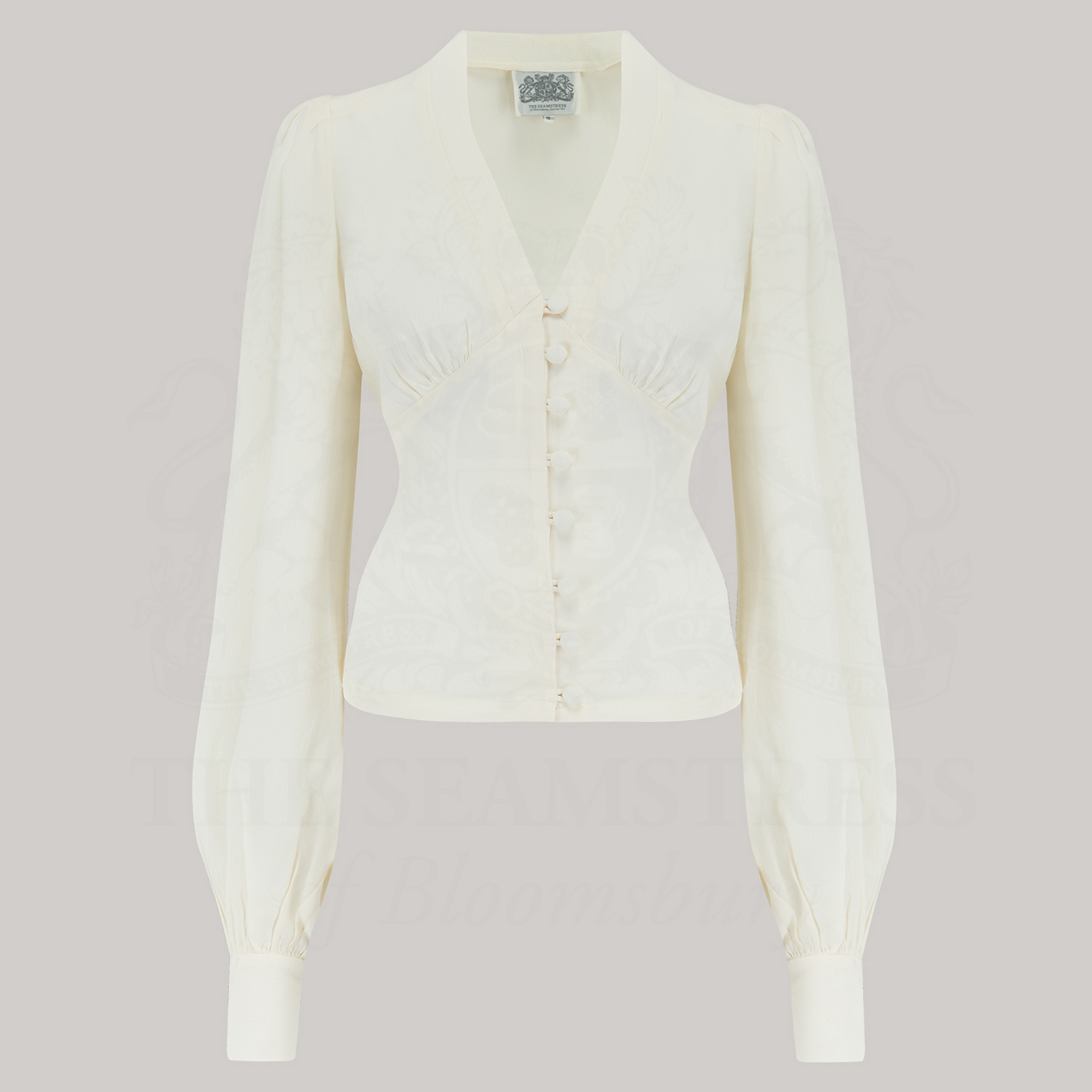 A cream-colored, long-sleeved blouse with a V-neckline and button details, 