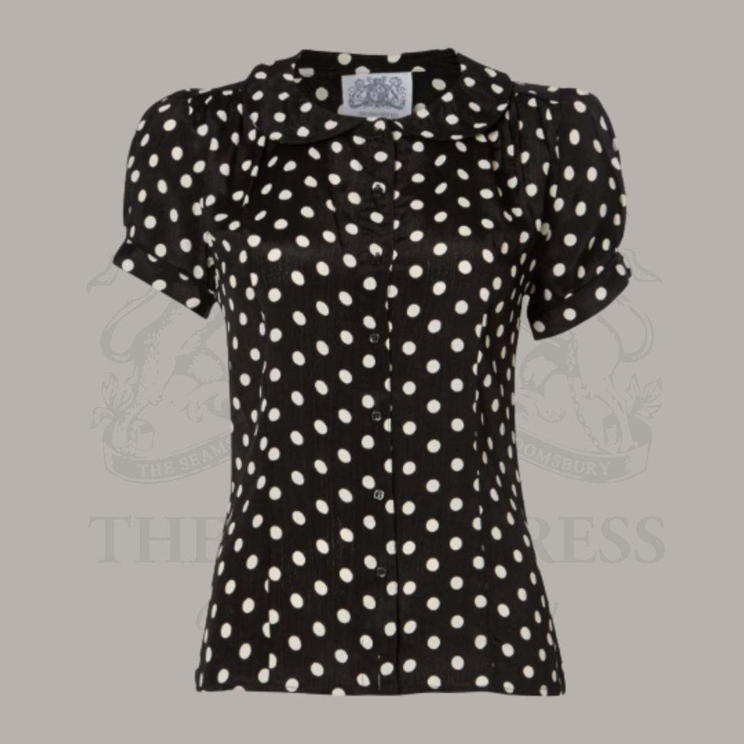 A black and white polka dot blouse with a Peter Pan collar and puff sleeves, displayed on a mannequin.