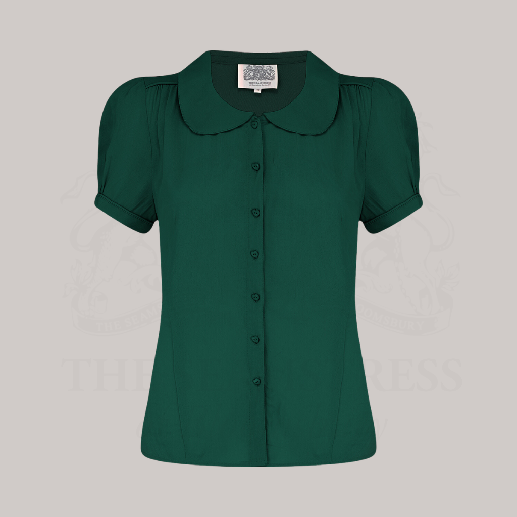 A green, short-sleeved blouse with a Peter Pan collar and front button fastenings.