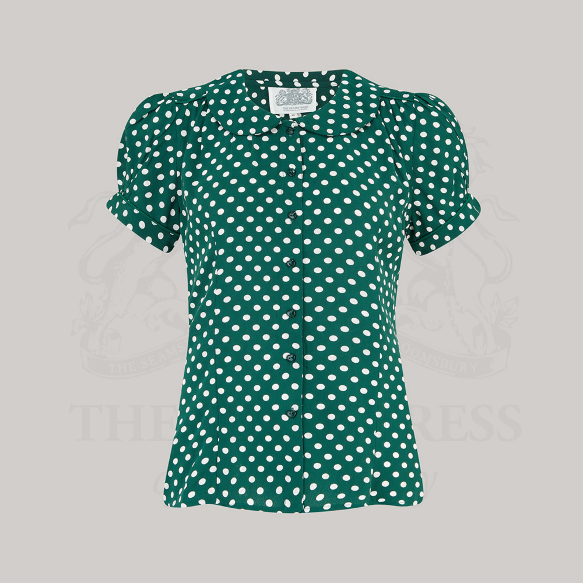 A short-sleeved green blouse with white polka dots, featuring a Peter Pan collar and fitted waist silhouette.