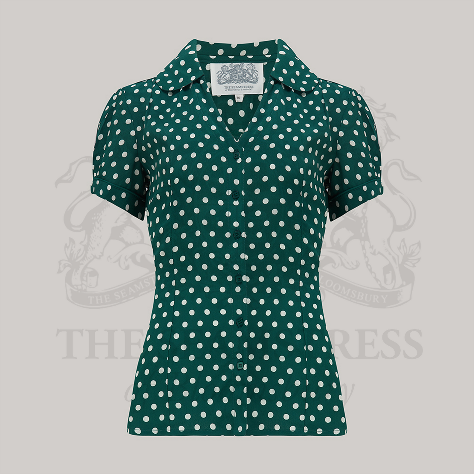 A vintage-style green blouse with white polka dots, featuring a Peter Pan-style collar and puff sleeves.