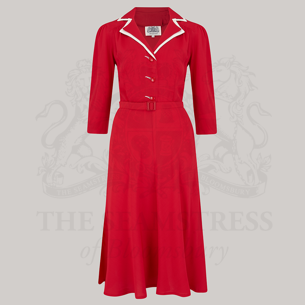 A red, knee-length shirtwaister dress with 3/4 length sleeves, square jet-style buttons, and a contrasting cream undercollar. 