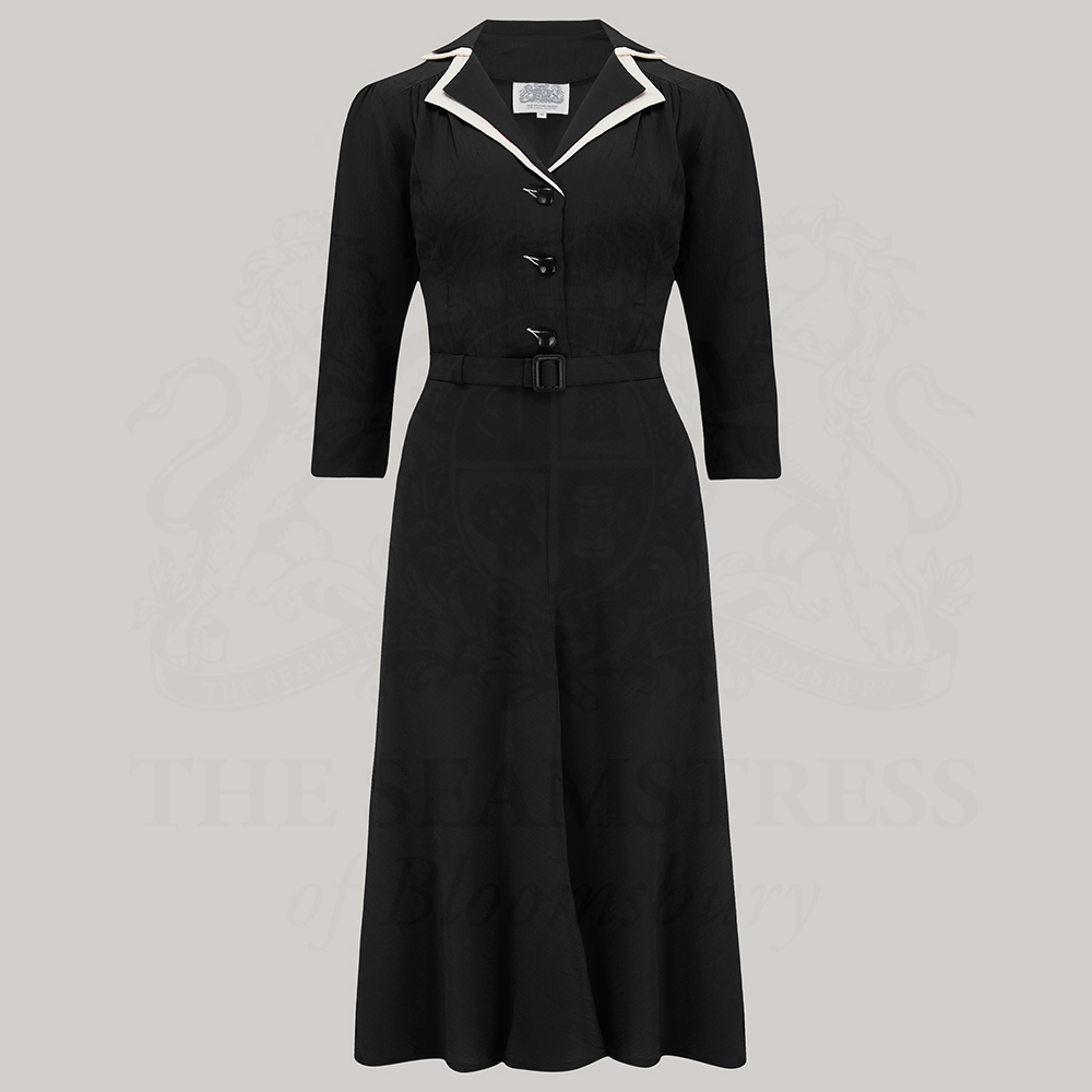 A classic black shirtwaister dress with contrasting cream undercollar and square jet-style buttons, featuring 3/4 length sleeves and side zip closure.