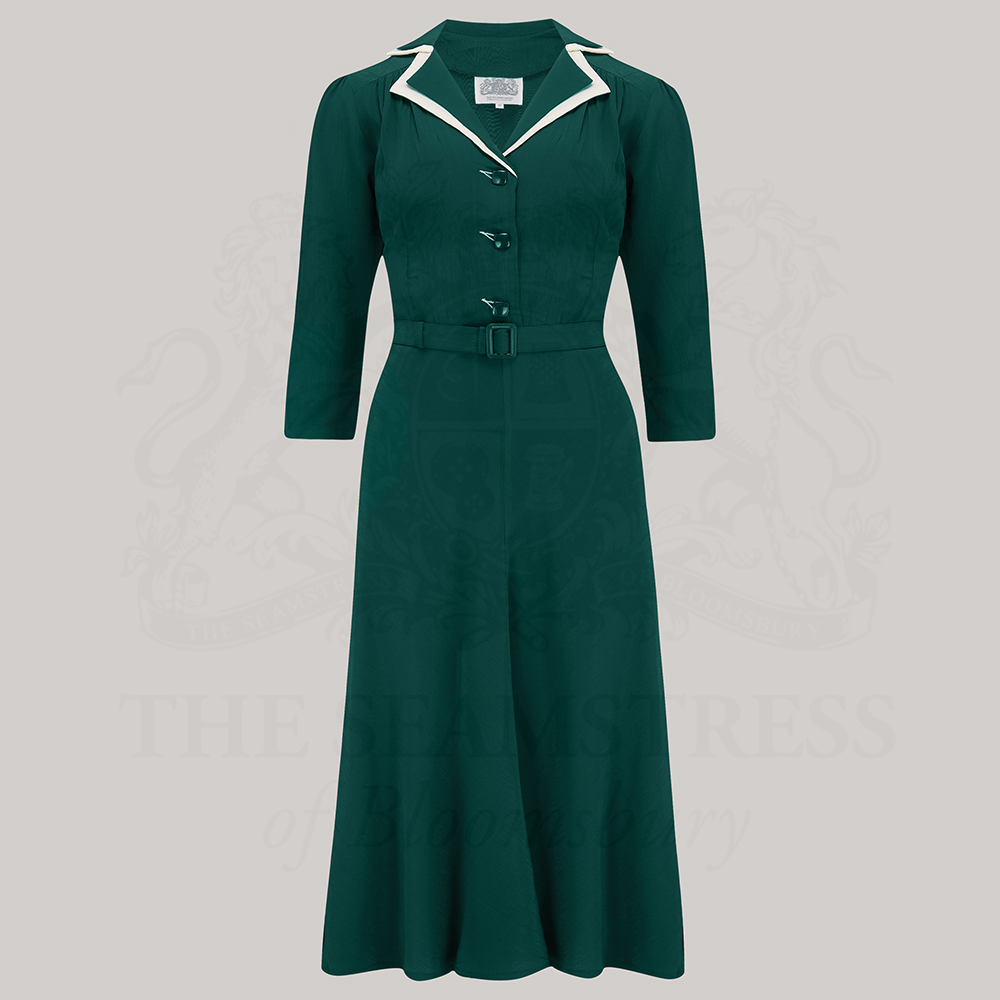 A green, knee-length shirtwaister dress with square jet-style buttons and a contrasting cream undercollar.