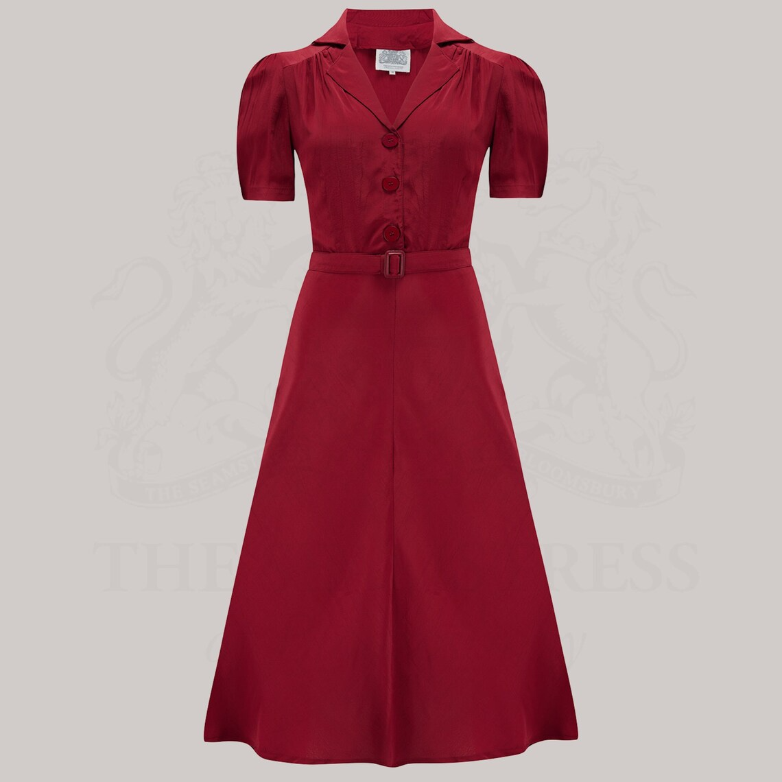 A red, short-sleeved shirtwaist dress with a button-down bodice and matching waist belt, made from crepe de chine fabric.