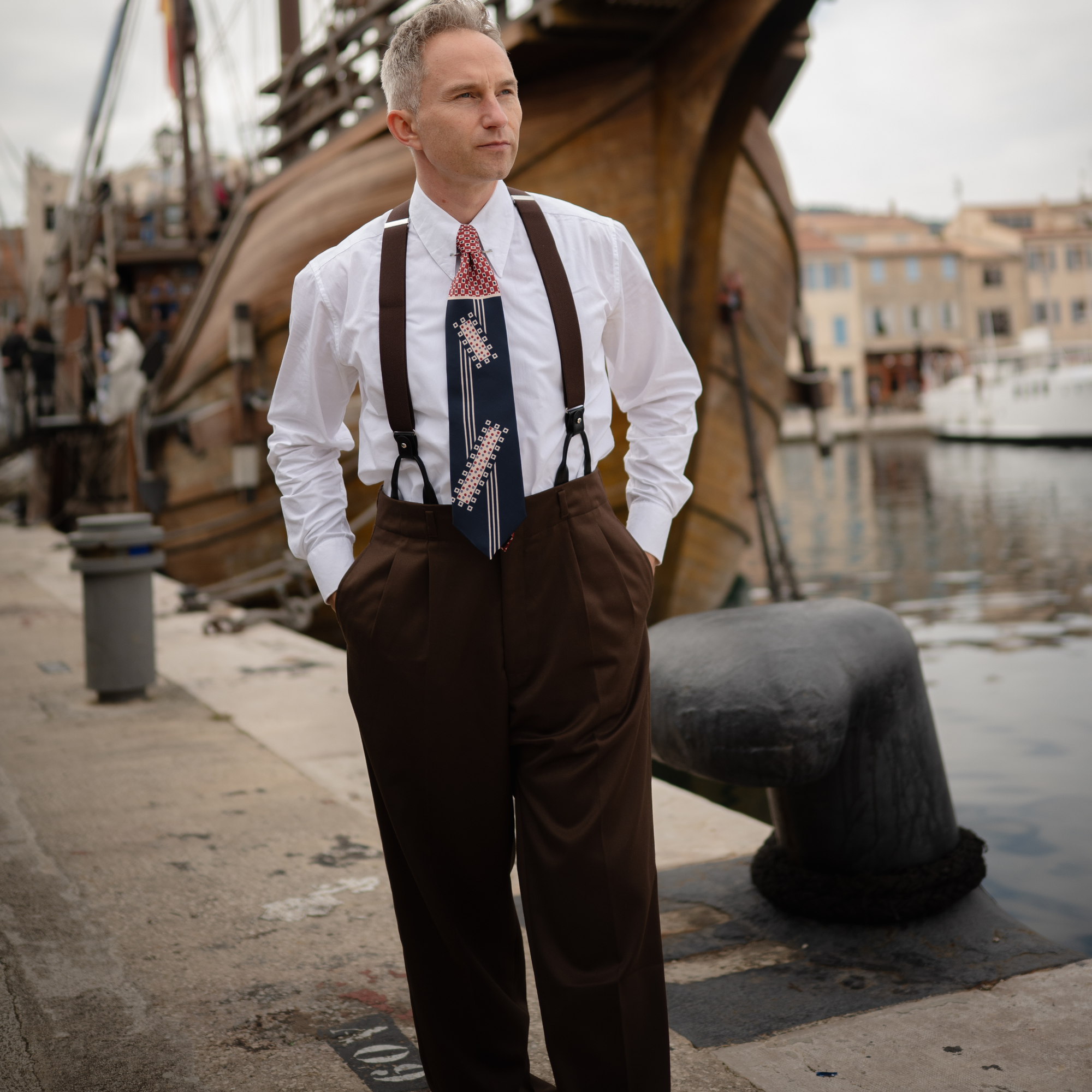 Man in vintage attire standing on a dock with a ship in the background