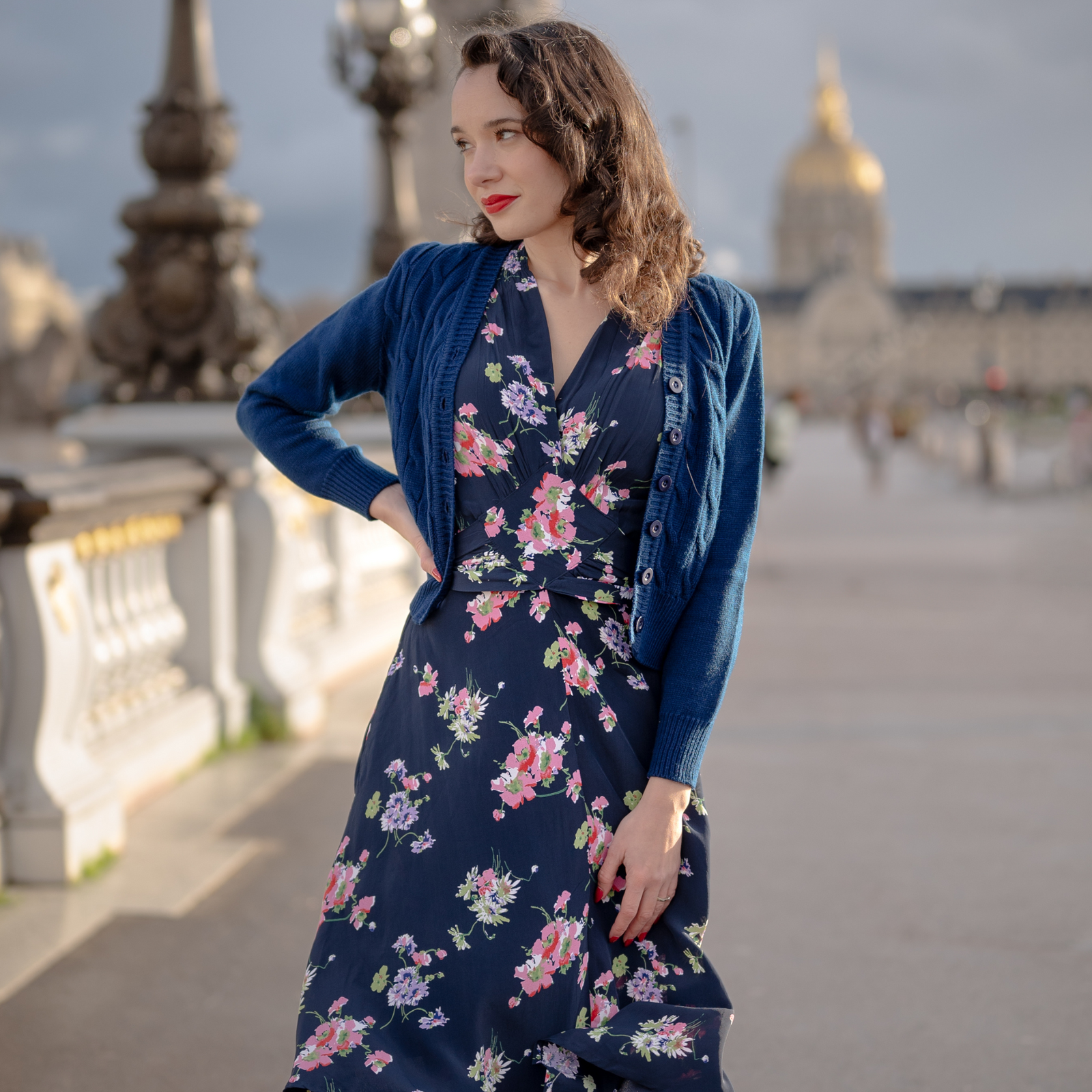 Model wears a navy blue 1940s-style cardigan on top of a navy floral dress. 