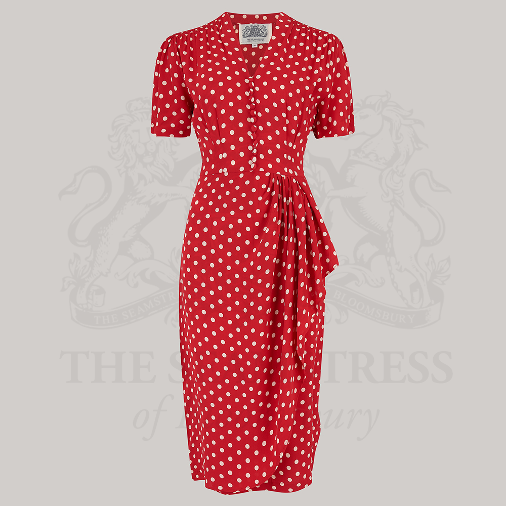 A red dress with white polka dots, featuring a fitted style with a waterfall ruffle on the waist and decorative buttons on the front bodice.