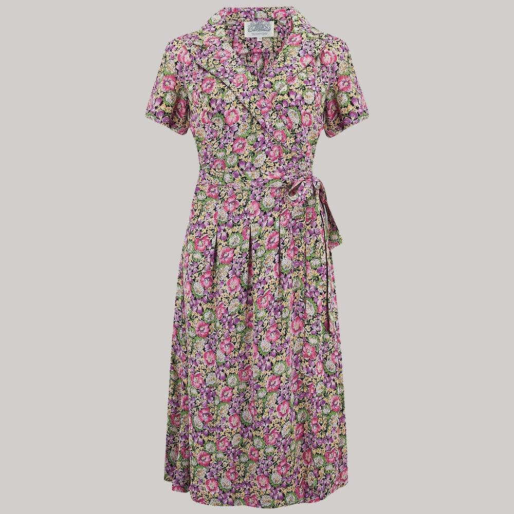 A short-sleeve wrap dress with a pink, purple, and green floral print, featuring a revere collar and a matching waist tie, shown against a solid light grey background.