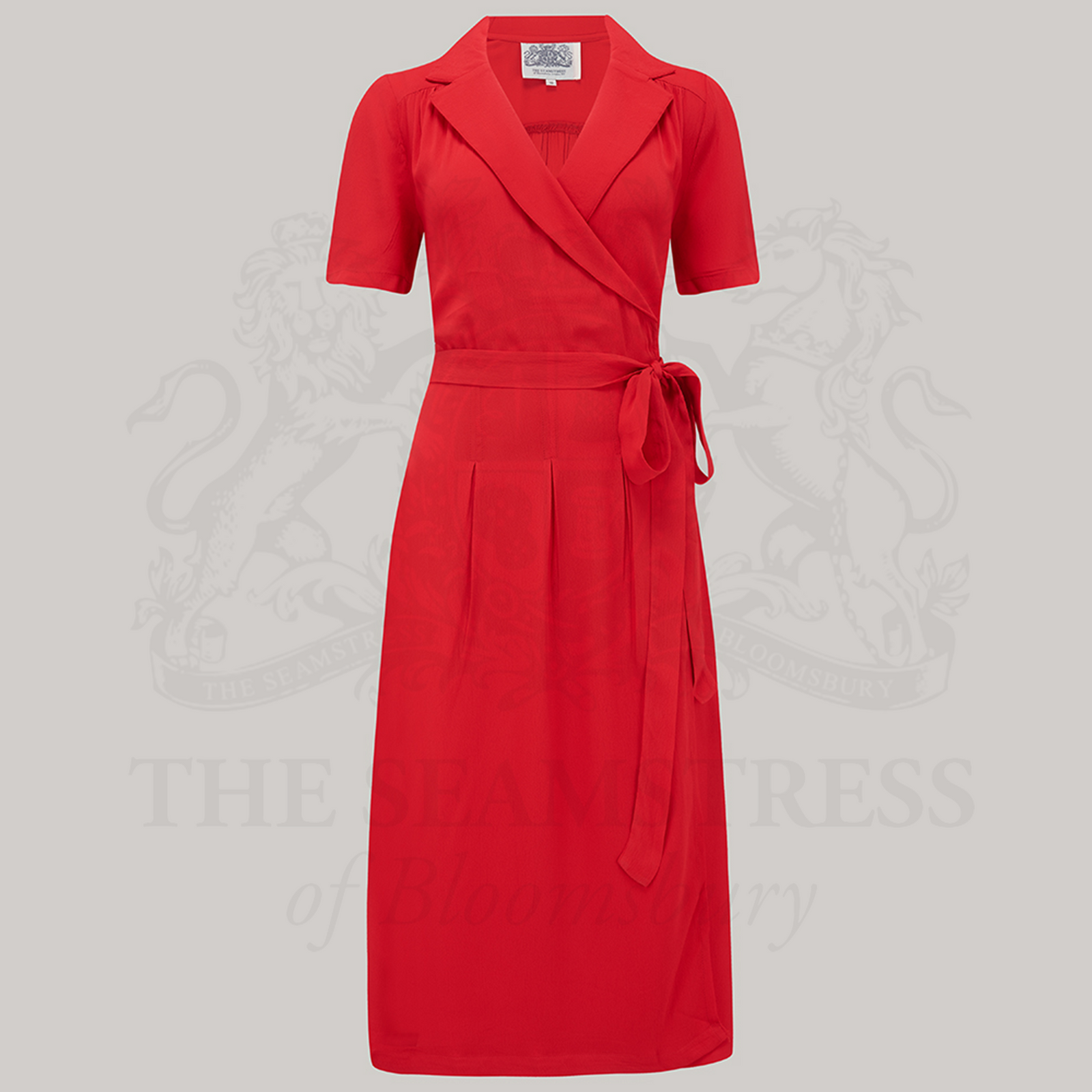 A red, short-sleeved Peggy wrap dress with a V-neck and tie at the waist, displayed against a grey background.