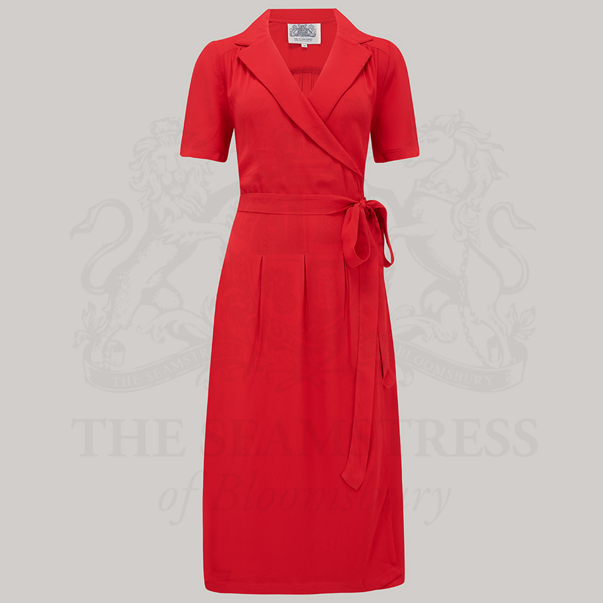 A red, short-sleeved Peggy wrap dress with a V-neck and tie at the waist, displayed against a grey background.