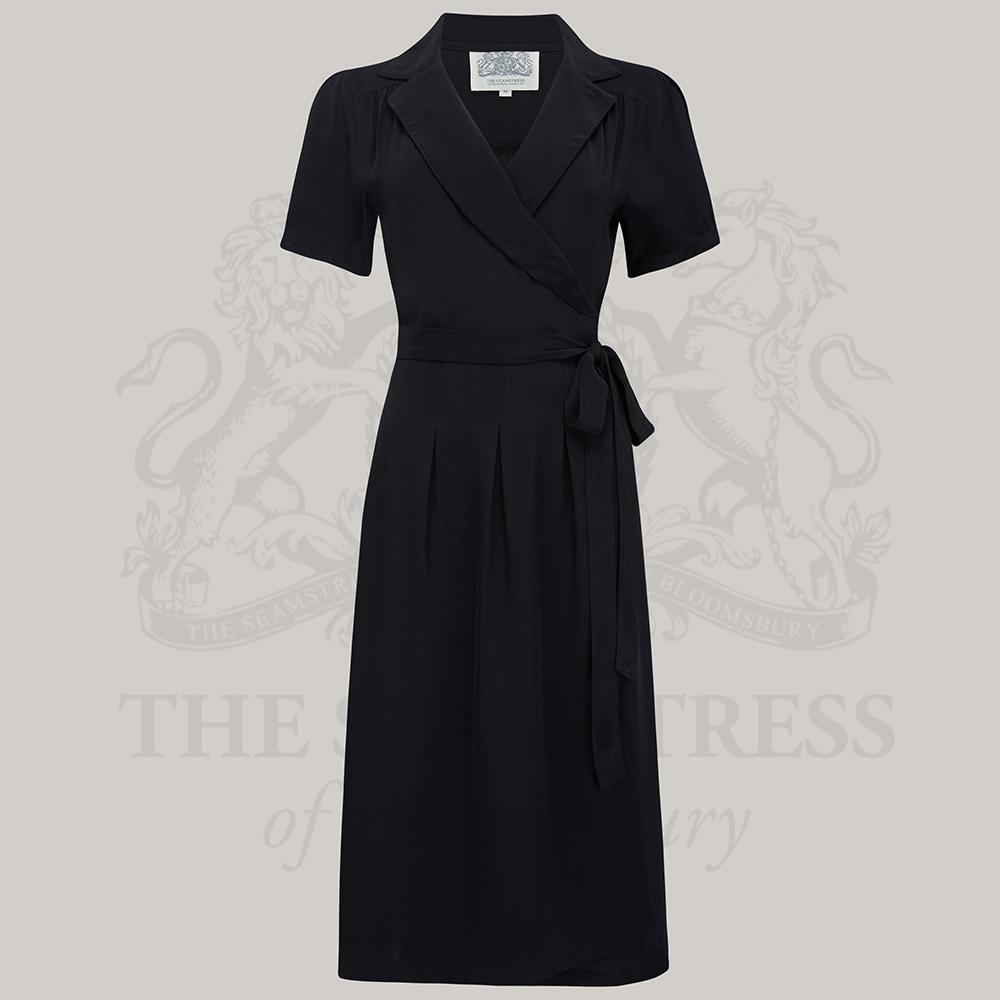 A black, short-sleeved Peggy Wrap Dress with a V-neck and tie at the waist, displayed against a grey background.