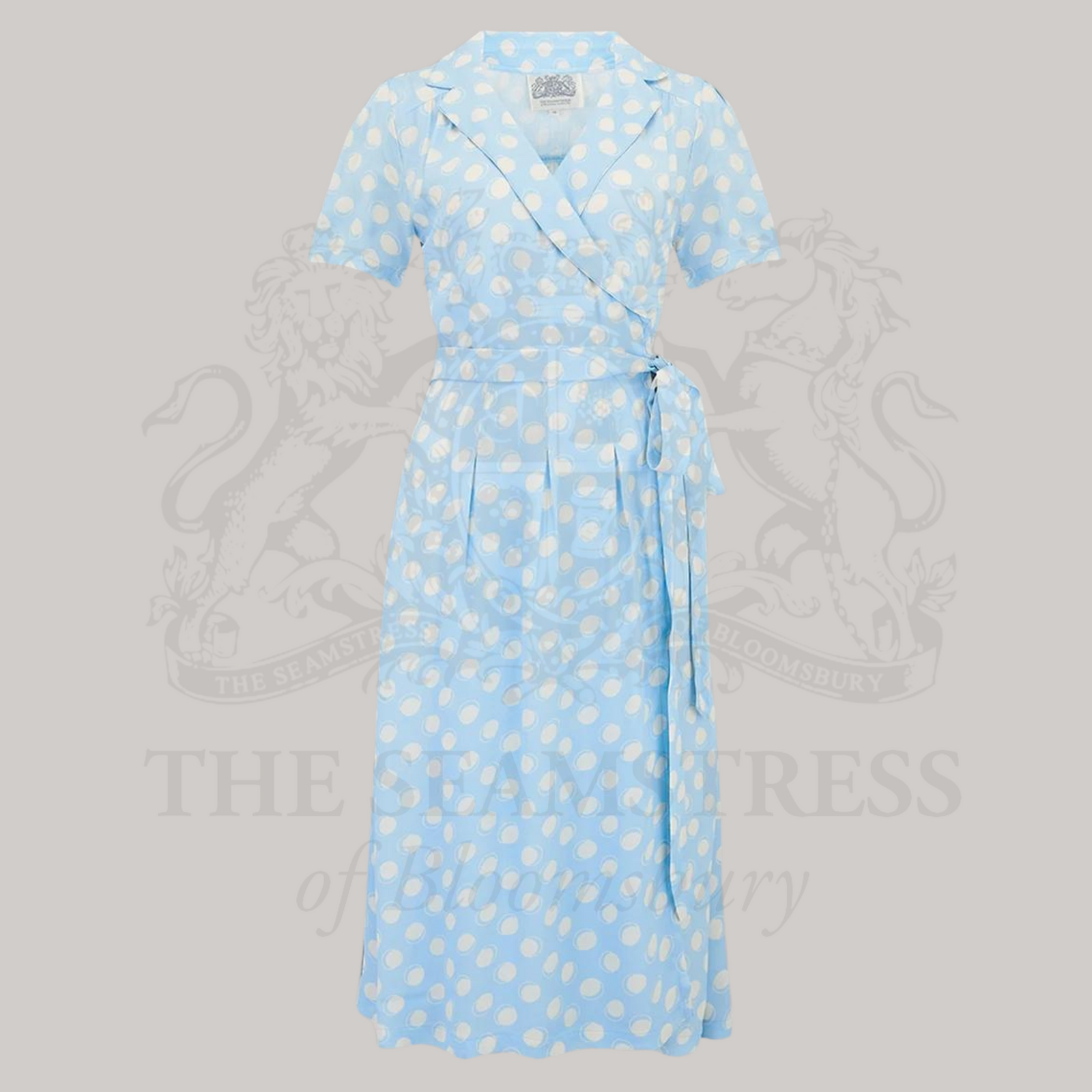 A powder blue wrap dress with polka dots, featuring a v-neck, tie at the waist, box pleats at the waistband, and side-seam pockets.