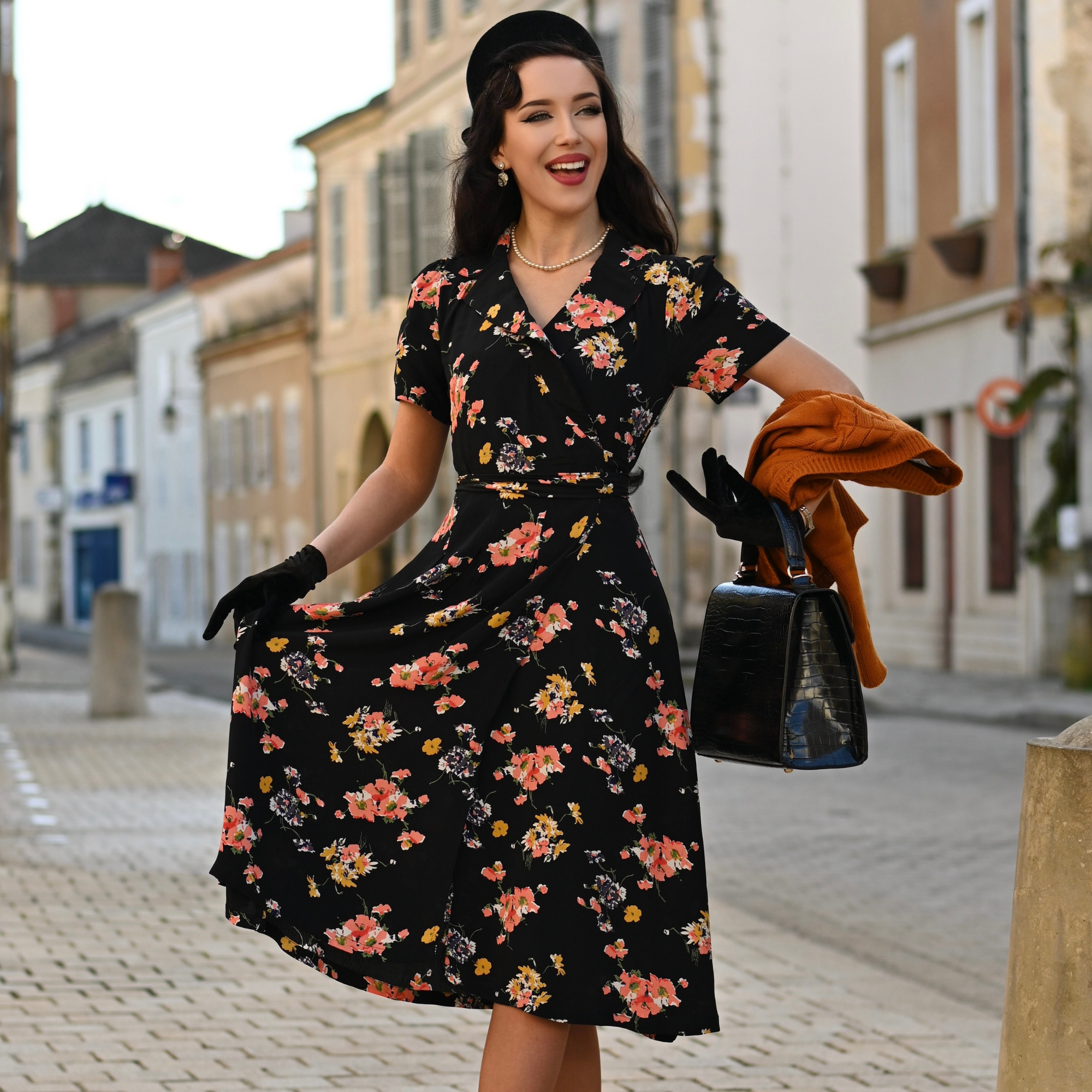A woman wearing a black mayflower wrap dress with a floral pattern, featuring a v-neck and short sleeves, standing on a street.