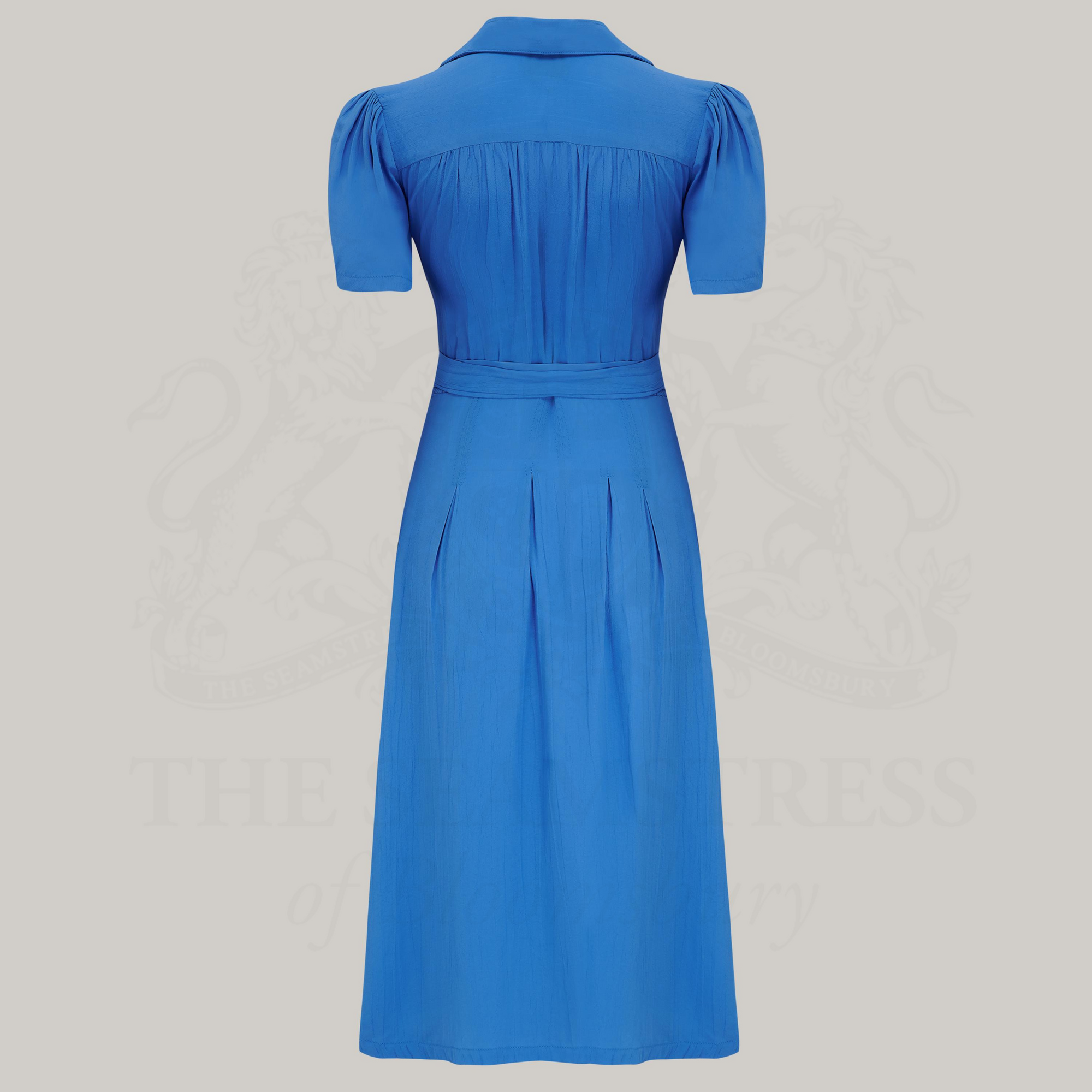 A blue v-neck dress with a tie at the waist, featuring box pleats at the waistband and side-seam pockets.