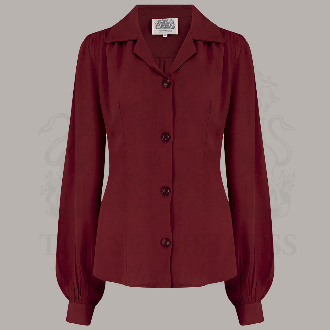 A red blouse with a revere collar, long sleeves with full cuffs, and subtle shoulder pads