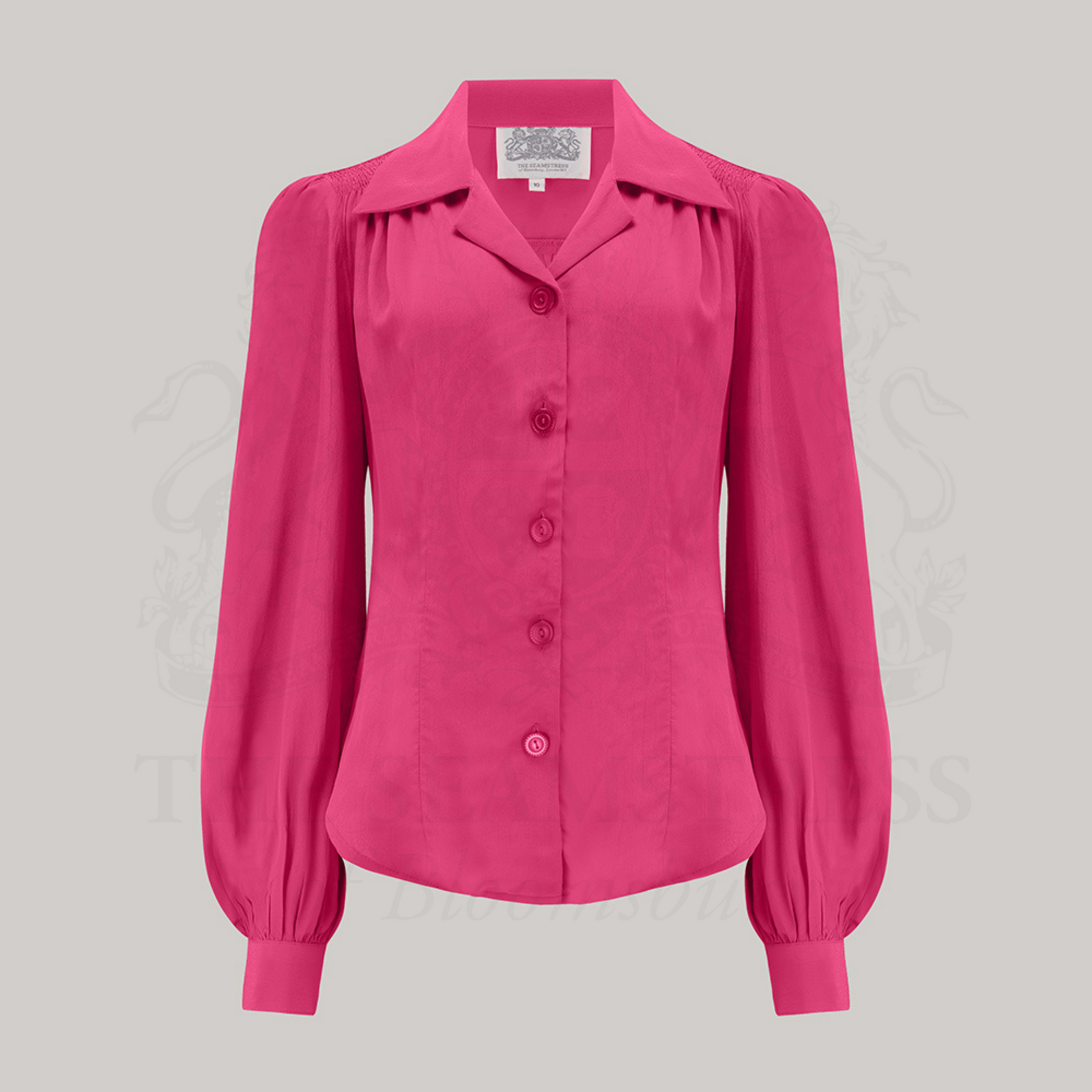 A raspberry blouse with a revere collar, long bishop sleeves with full cuffs, and a fitted waist. The blouse features shoulder pads and is made from Crepe de Chine fabric.