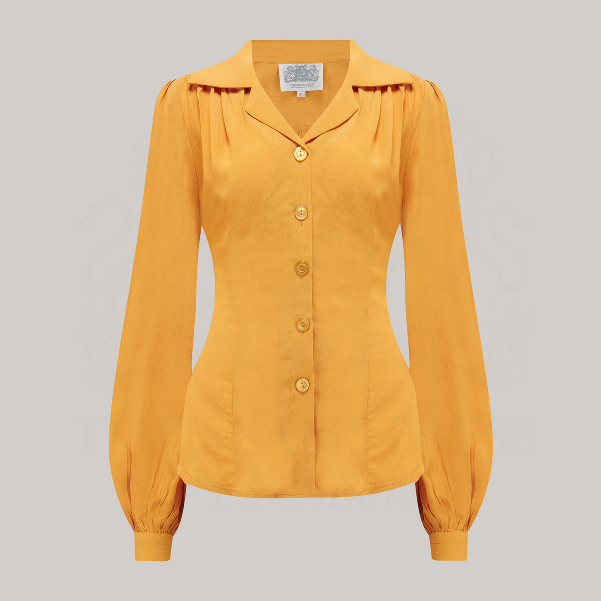 A mustard yellow blouse with a revere collar and long bishop sleeves