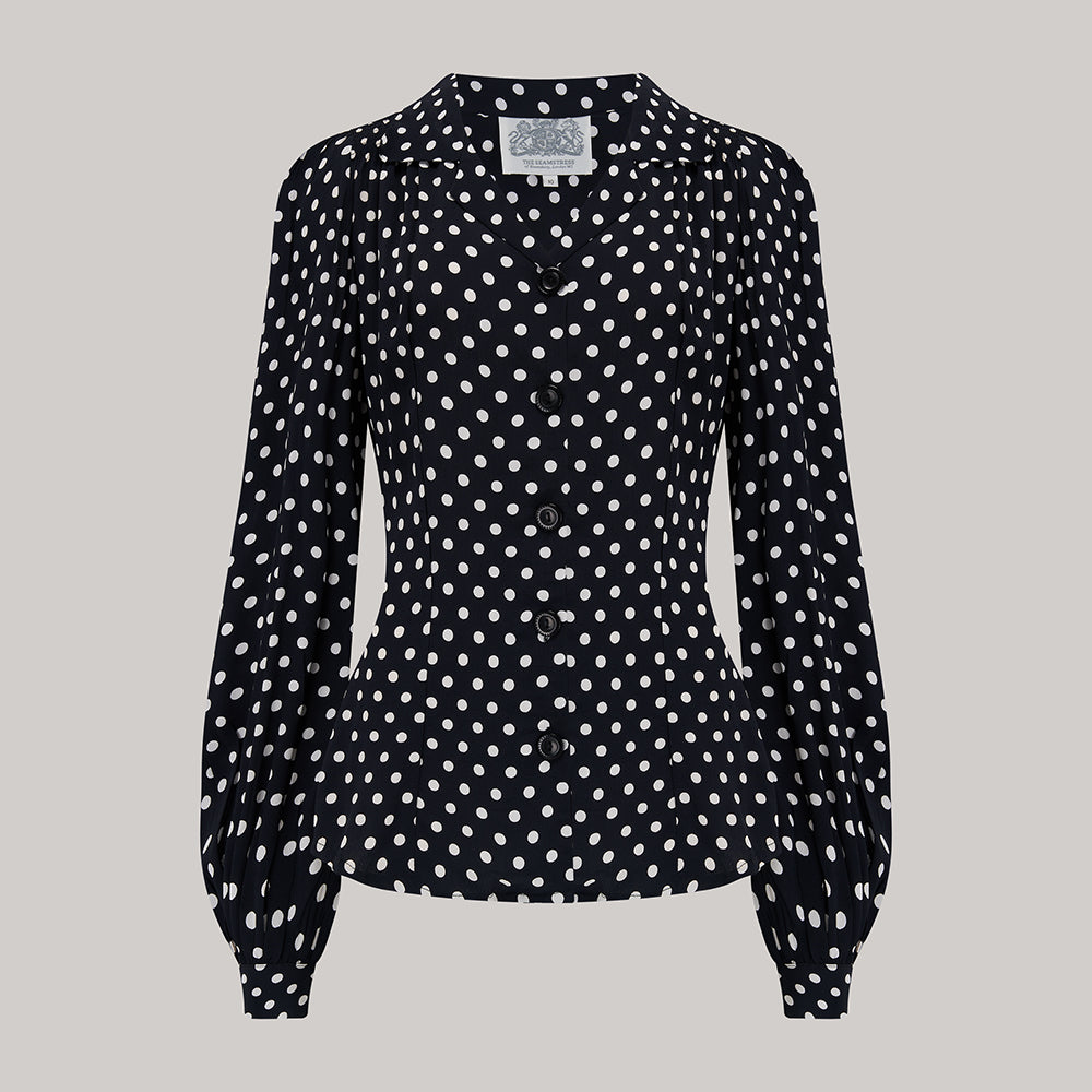 A black and white polka-dot blouse with a revere collar, long sleeves with full cuffs, and shoulder pads.