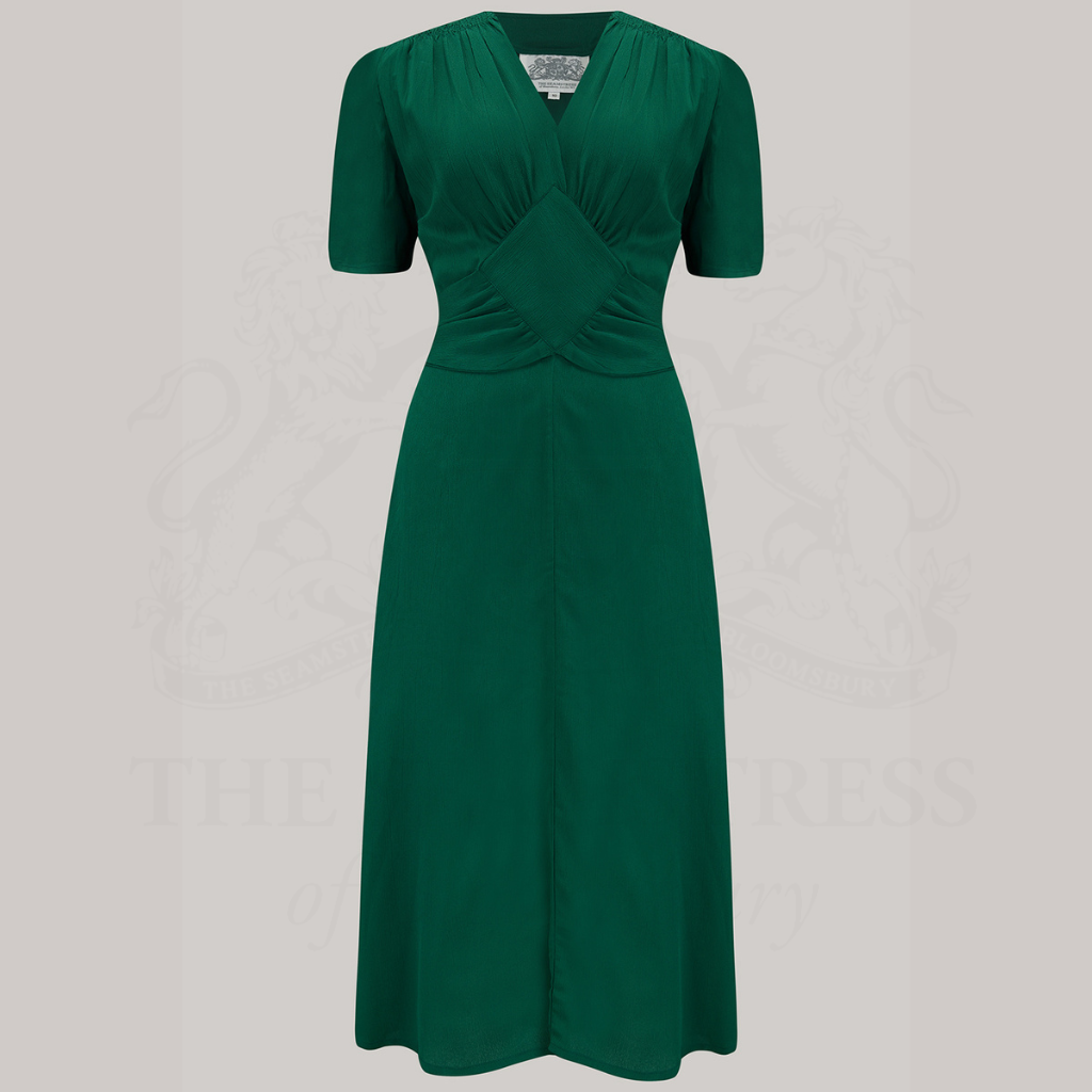 A green knee-length dress with shoulder smock detailing, a diamond-shaped bodice, and side pockets.