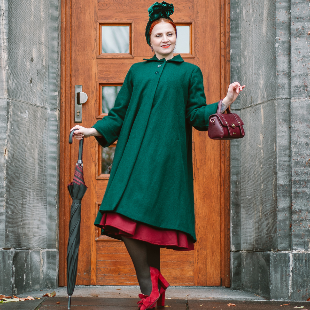 model wearing a long 1940s style coat in dark green. 