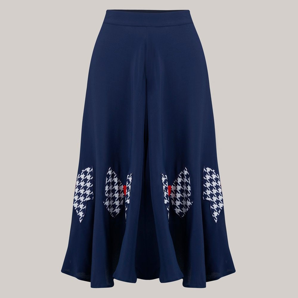 A navy blue wide-leg midi skirt with three large houndstooth-patterned bow patches near the hem, accented with small red details, shown against a solid light grey background.