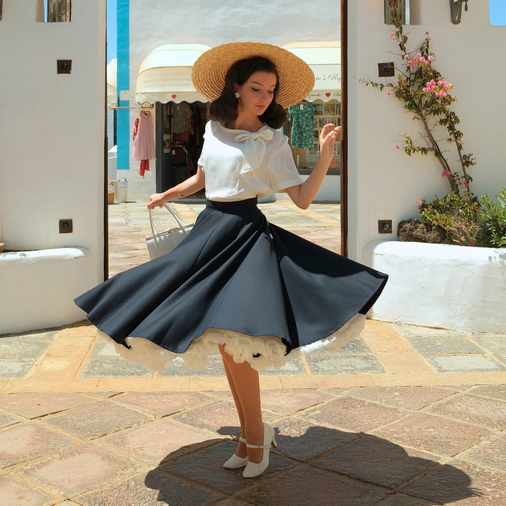 A woman wearing a navy skirt and cream blouse twirling in front of a stone building.