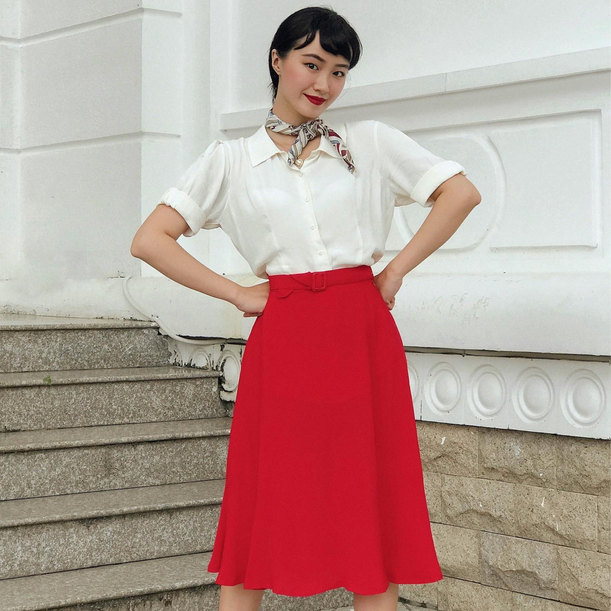 Model wears a 1940s-style red circle skirt with a short-sleeved cream blouse and a necktie.