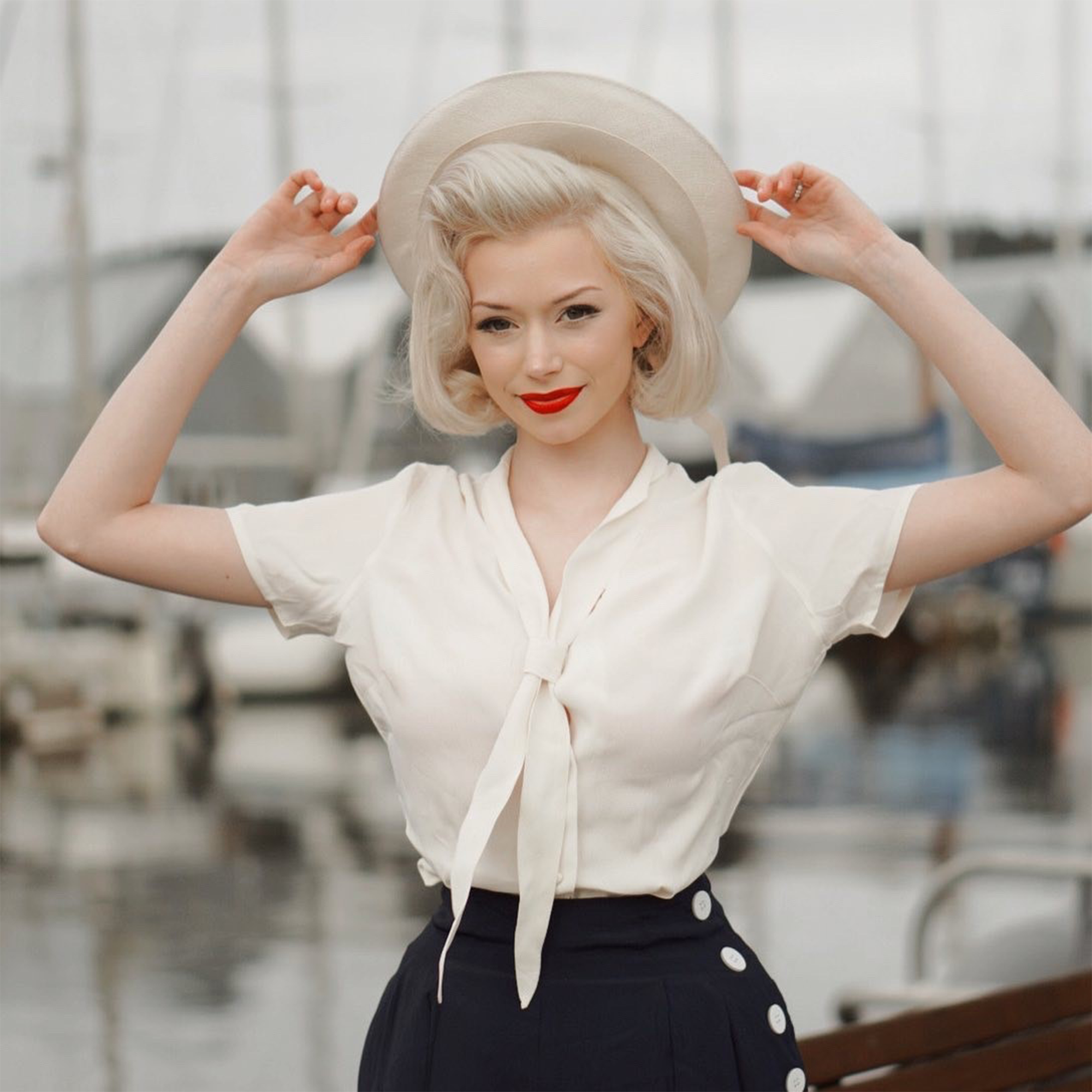 Model wears a 1940s sailor style blouse with short sleeves in cream with black wide-leg women’sTrousers and a matching cream hat.