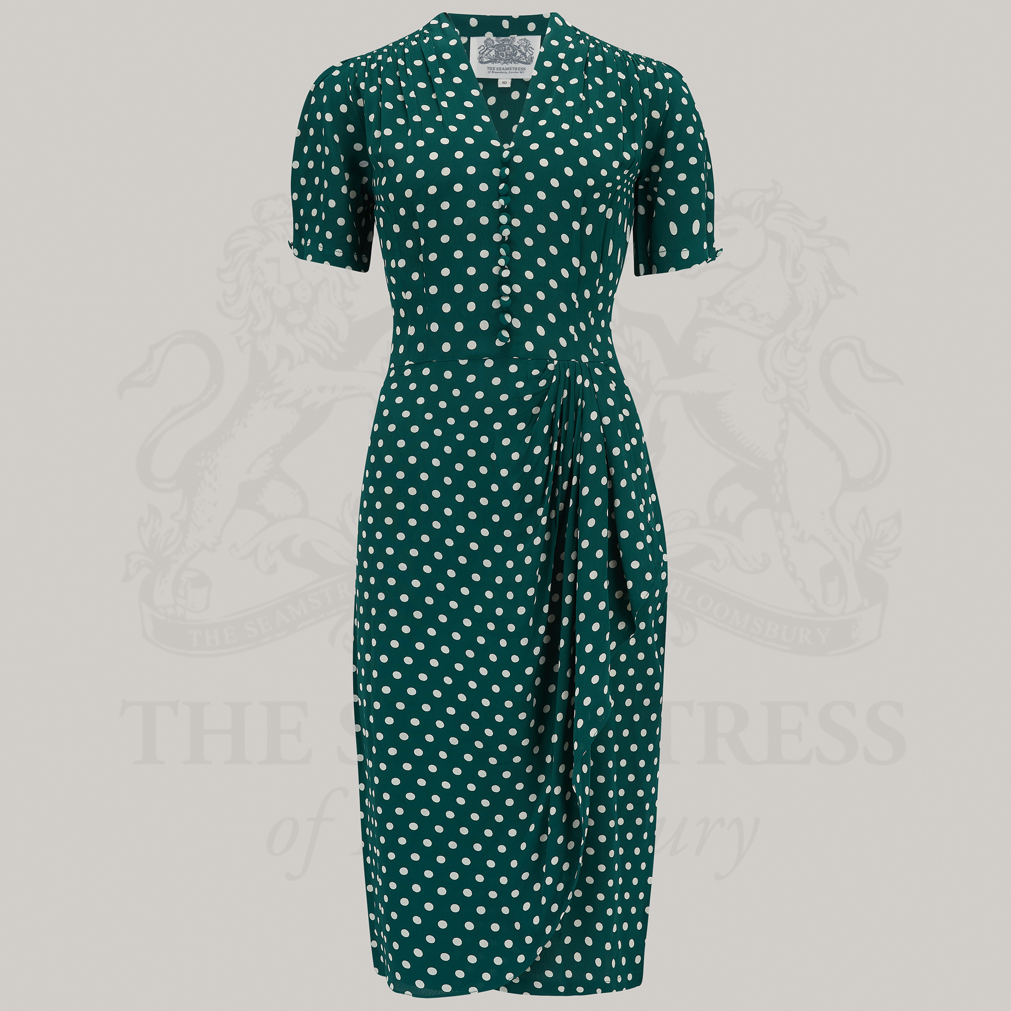 A green polka-dot dress with a fitted style, waterfall ruffle on the waist, and decorative buttons on the front.
