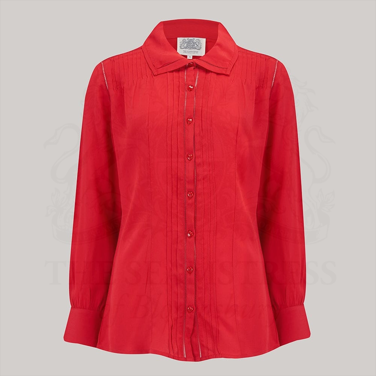 A 1940s style red long sleeve blouse. Detailed pin tuck stitching down the front and back of the blouse, heart shaped buttons, and long sleeves with deep cuffs. Blouse has a cutaway collar with more pin tuck stitching. 