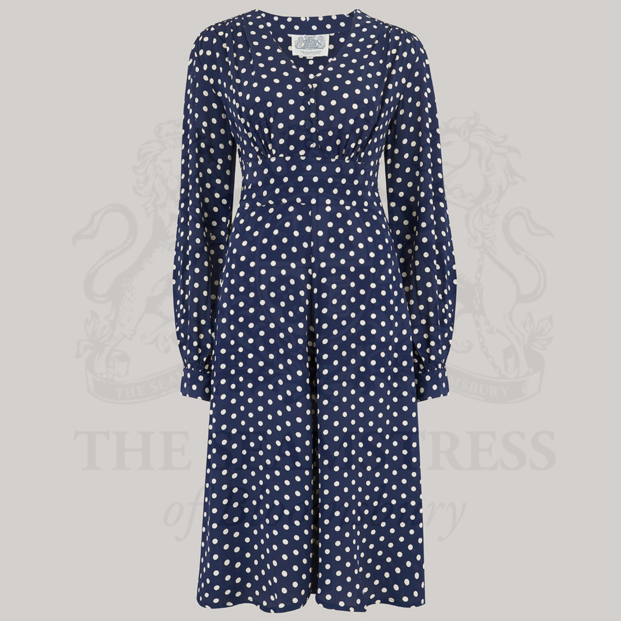 A 1940s style long sleeve dress in navy with cream polka dots. Featuring gauged-in top yoke detailing on the shoulders and sleeves that puff out fully at the cuff. 4 small buttons down the front of the dress, and a tie-waist belt. 
