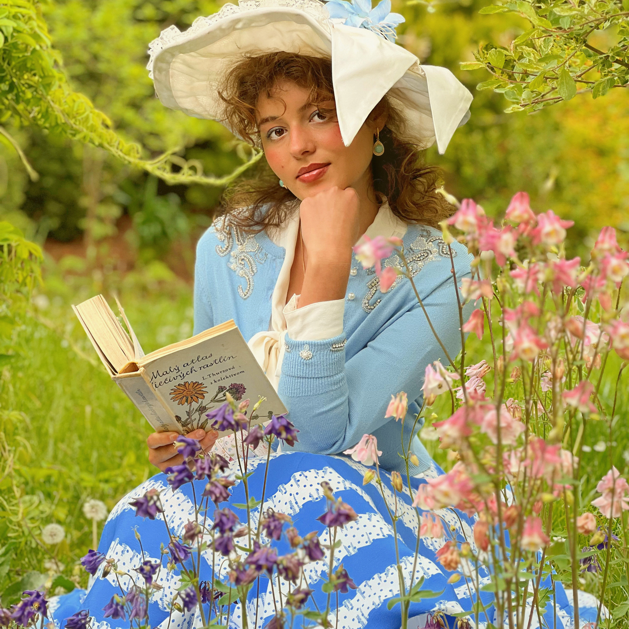 Woman in vintage attire reading a book in a garden