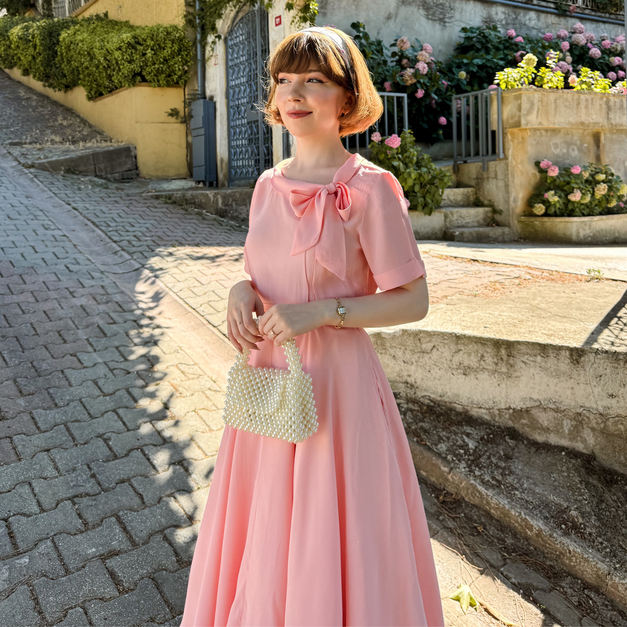 Model wears a pale pink short-sleeved 1940s-style dress with a side bow collar.