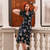 Model wears a 1940s-style swing dance dress in navy blue with a floral pattern. Model also wears black netted gloves and matching black heels. 