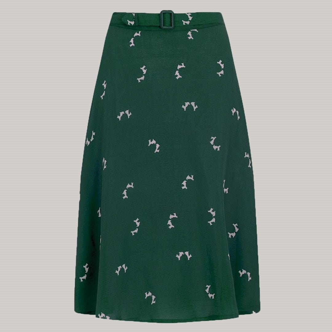 A dark green skirt with a repeating white pattern of small dogs, featuring a matching belt with a dark buckle, shown against a solid light grey background.