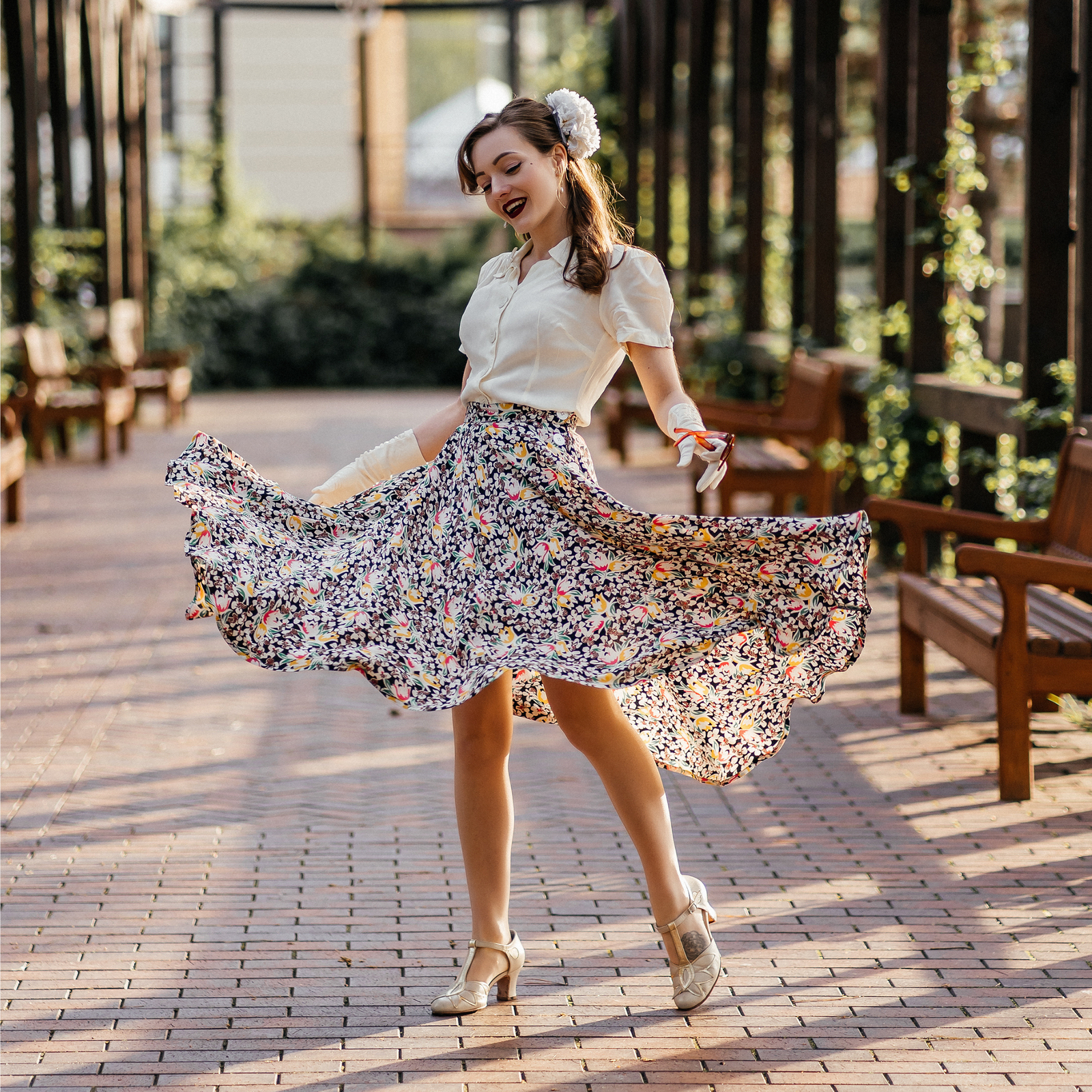 Woman in a floral skirt and white blouse twirling outdoors on a sunny day.