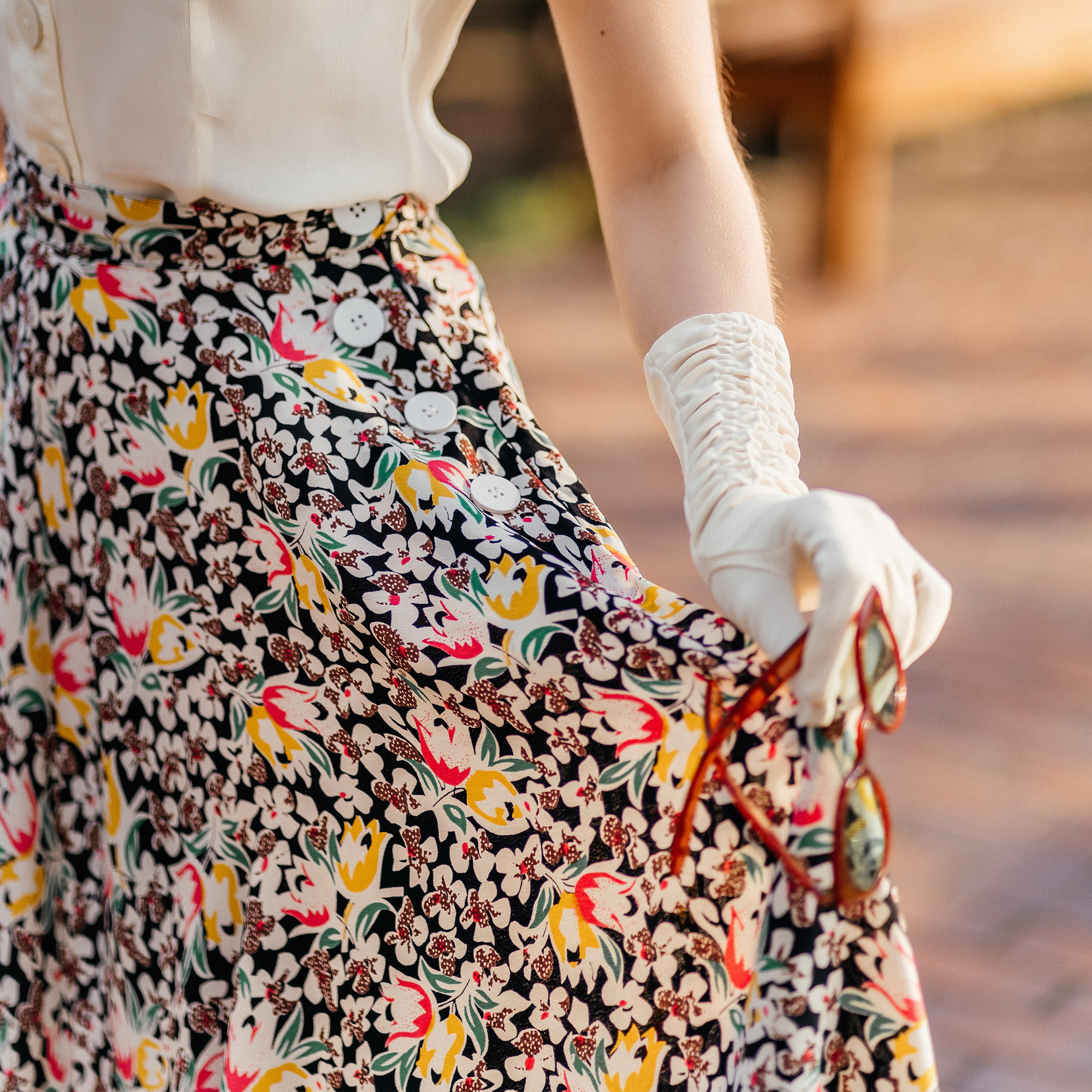 Person wearing a floral skirt with colorful patterns and a white glove.