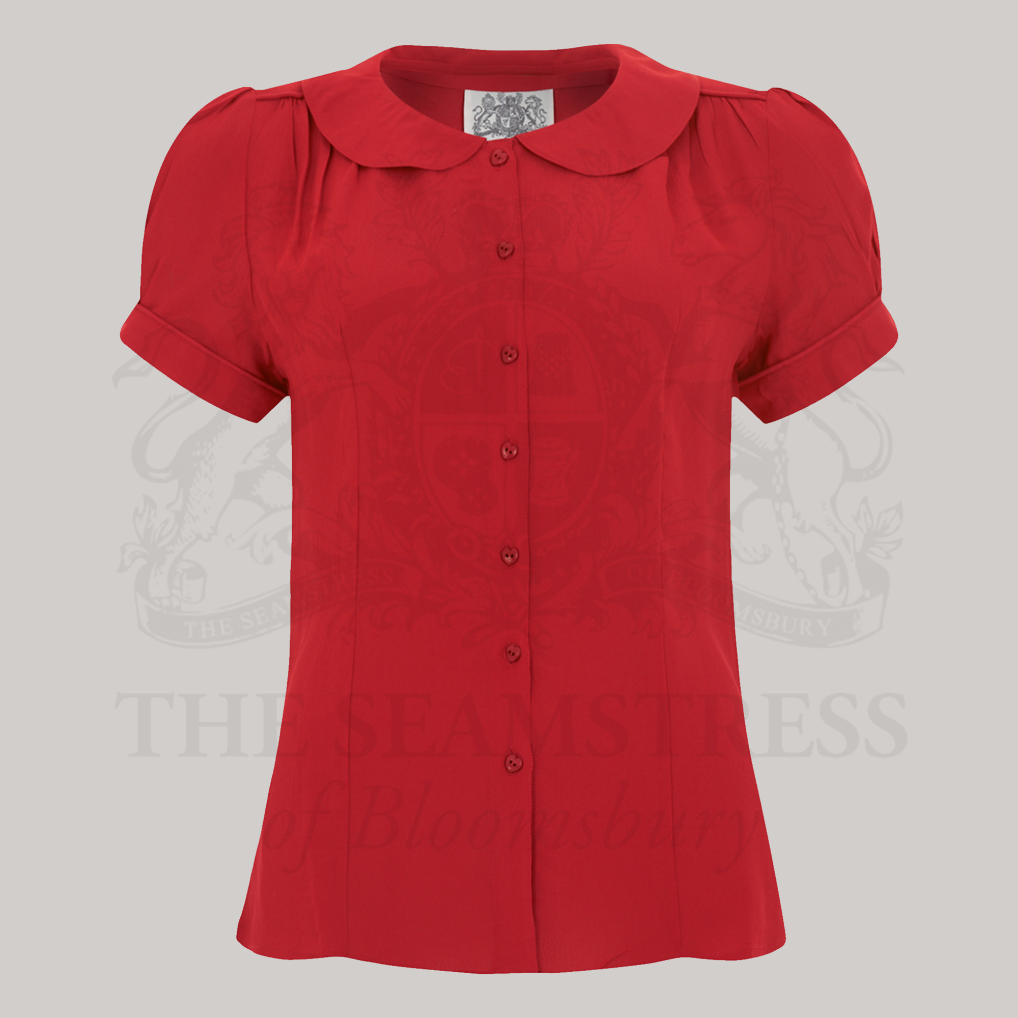 A woman in a red short-sleeved blouse with a Peter Pan collar and puff sleeves, standing next to a red suitcase