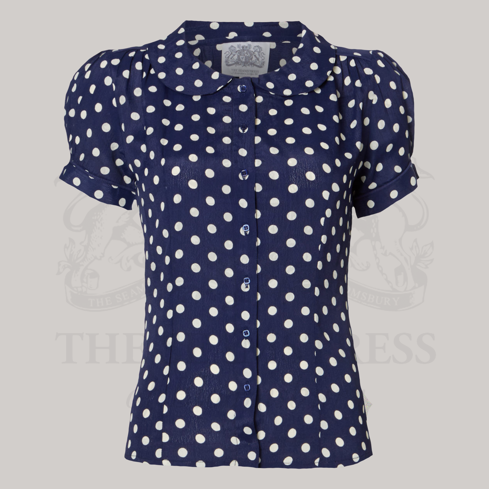 A navy blouse with white polka dots featuring a Peter Pan collar and short puff sleeves, with front button fastenings.