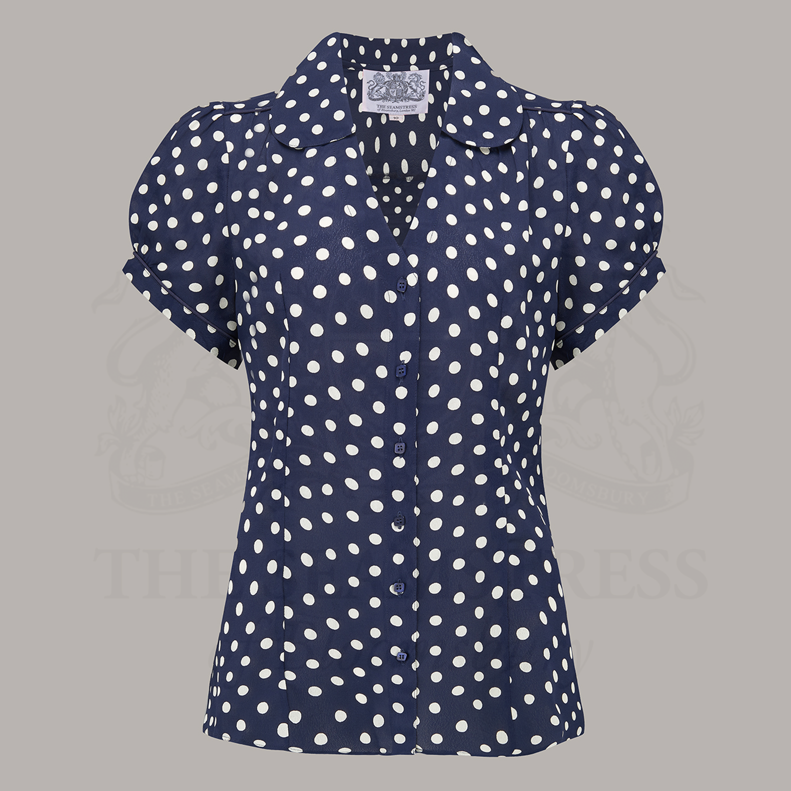 A navy blouse with white polka dots featuring a Peter Pan-style collar, puff sleeves, and V-front fastening with buttons.