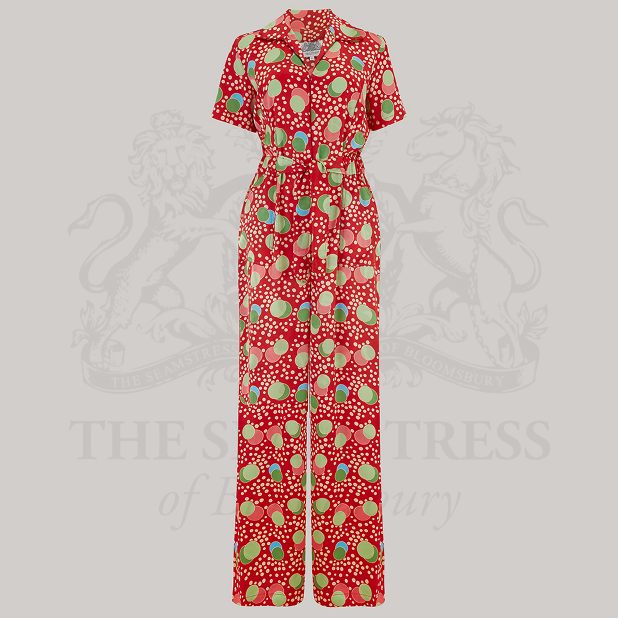 A red satin jumpsuit with a colorful floral pattern, featuring short turn-back sleeves, a revere collar, slant side pockets, and an elasticated waist with a front tie belt.