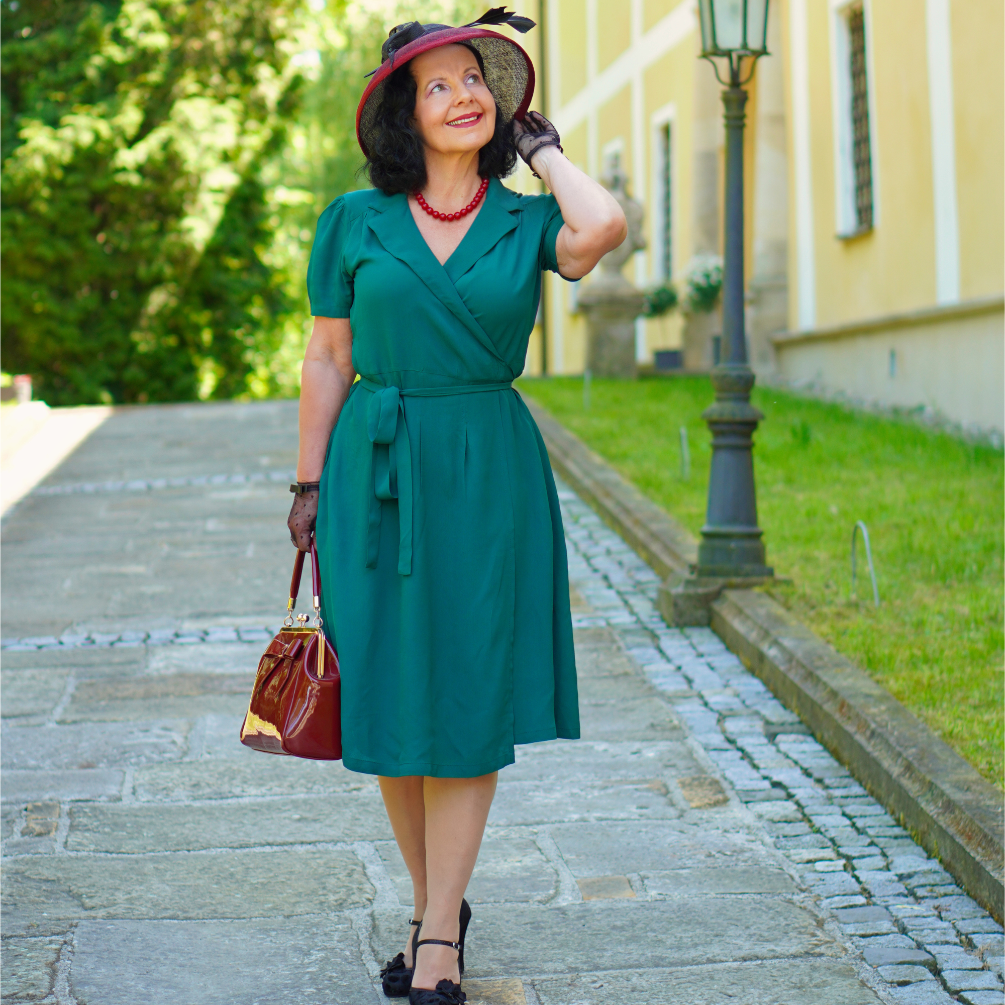 Woman in a green dress standing on a stone path with greenery and a building in the background