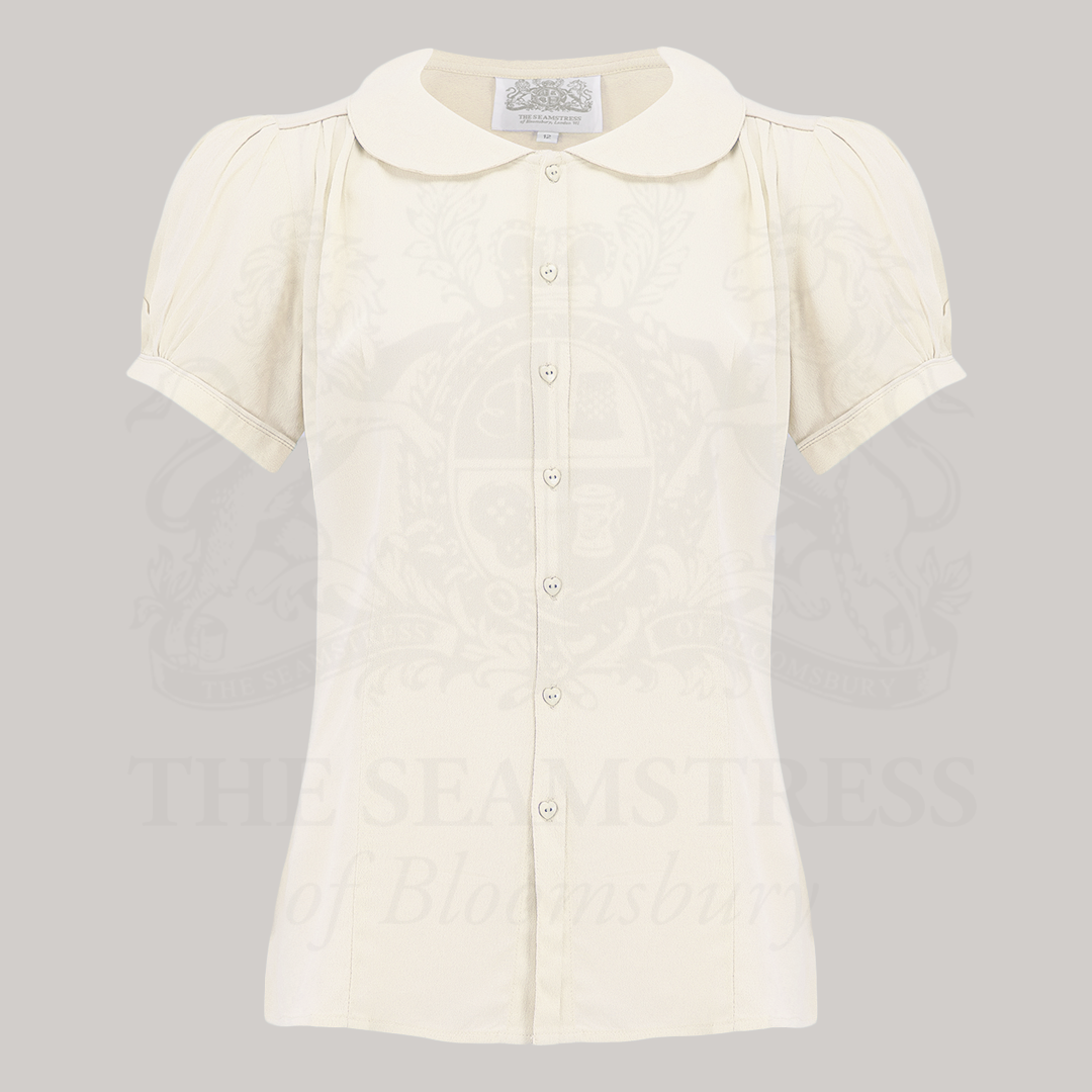 A cream-coloured short-sleeved blouse with a Peter Pan collar and puff sleeves,