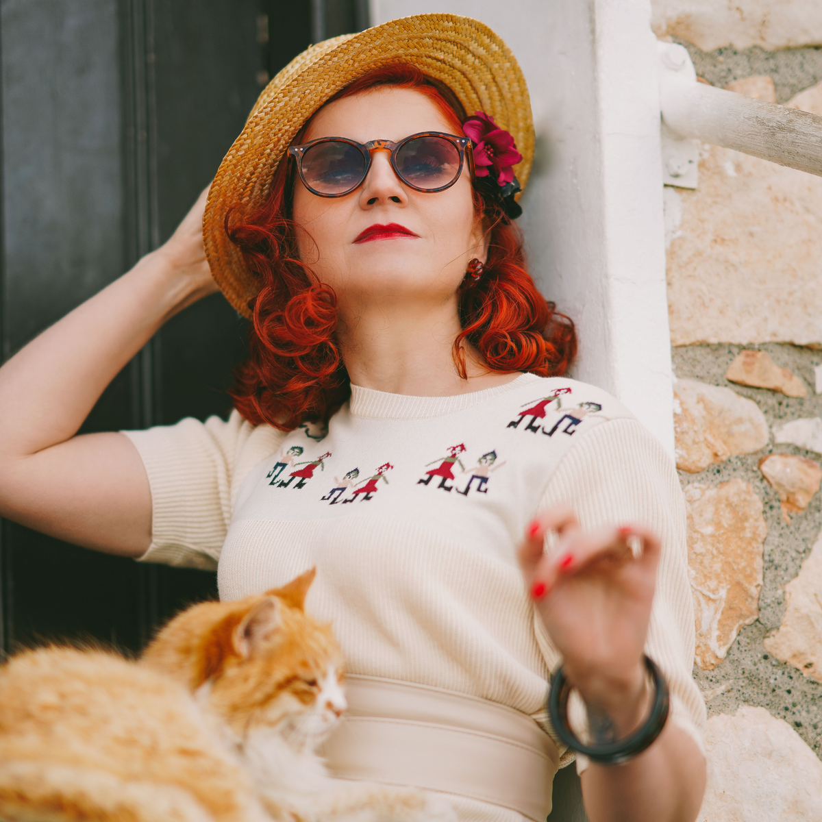 Model wears knitted cream jumper with half-length sleeves and small figures along the chest. Accessorised with a summer straw hat and 1940s style sunglasses. 