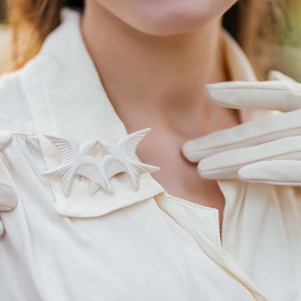 An acrylic brooch in the shape of two bluebirds, pinned on the collar of a cream blouse