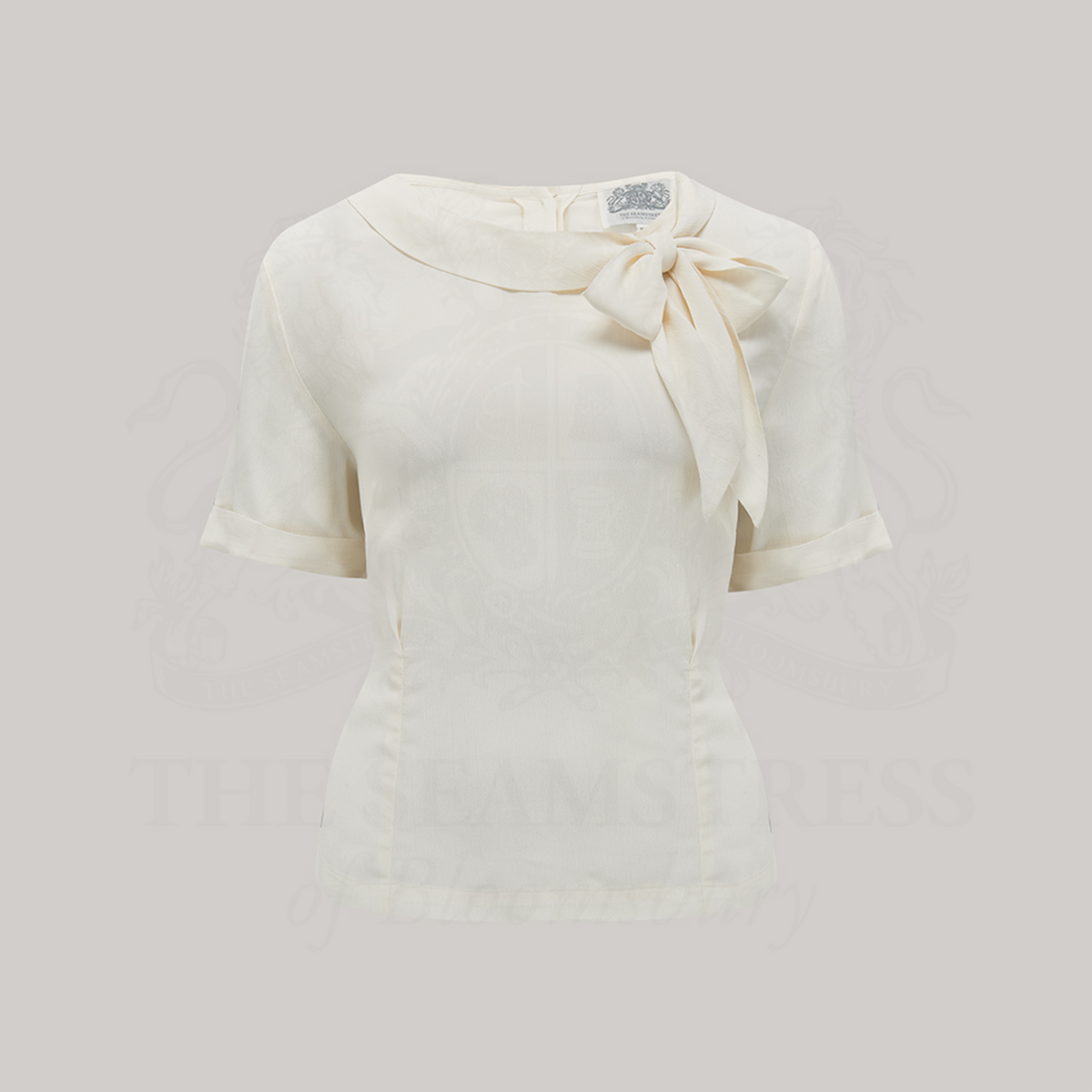 A 1940s style short sleeve cream blouse. Featuring a side tie-neck collar and button fastenings down the back of the blouse.