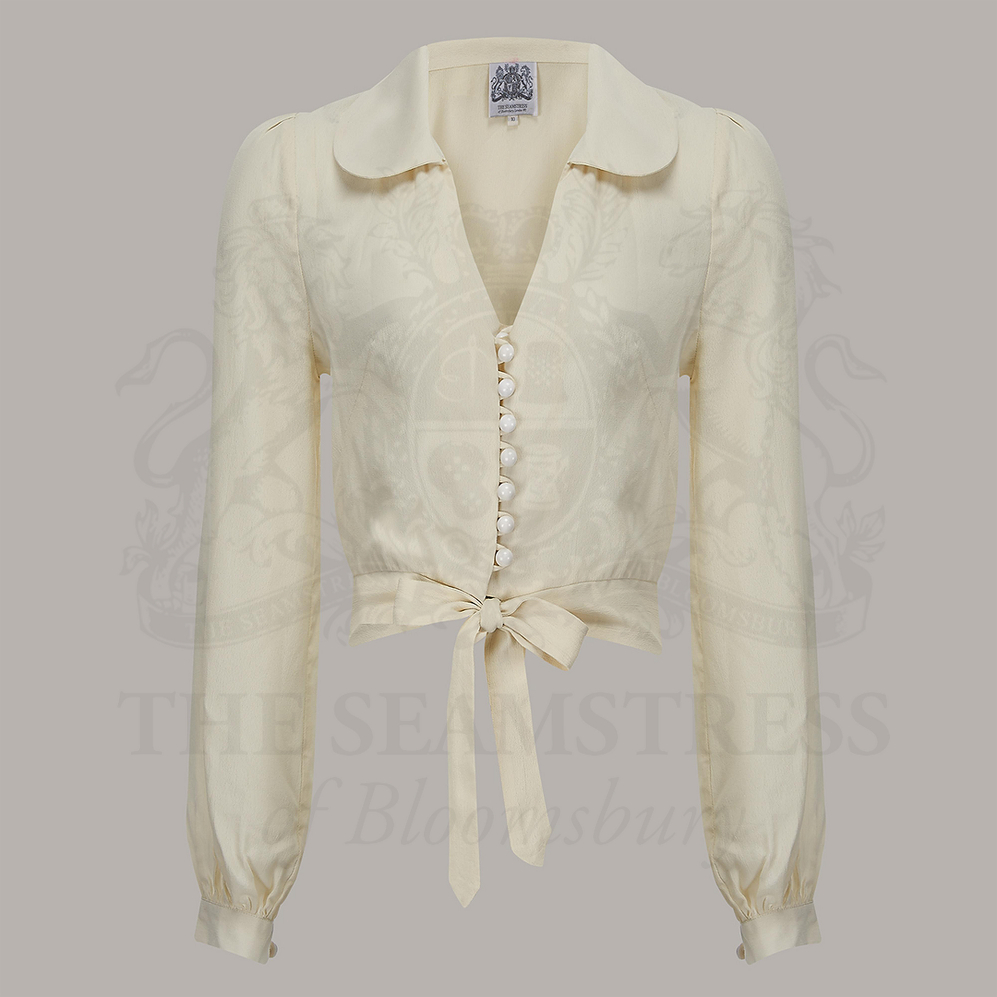 A 1940s-style long-sleeve blouse in cream. The blouse has a v-neck, button fastenings on the front, and a waist tie.